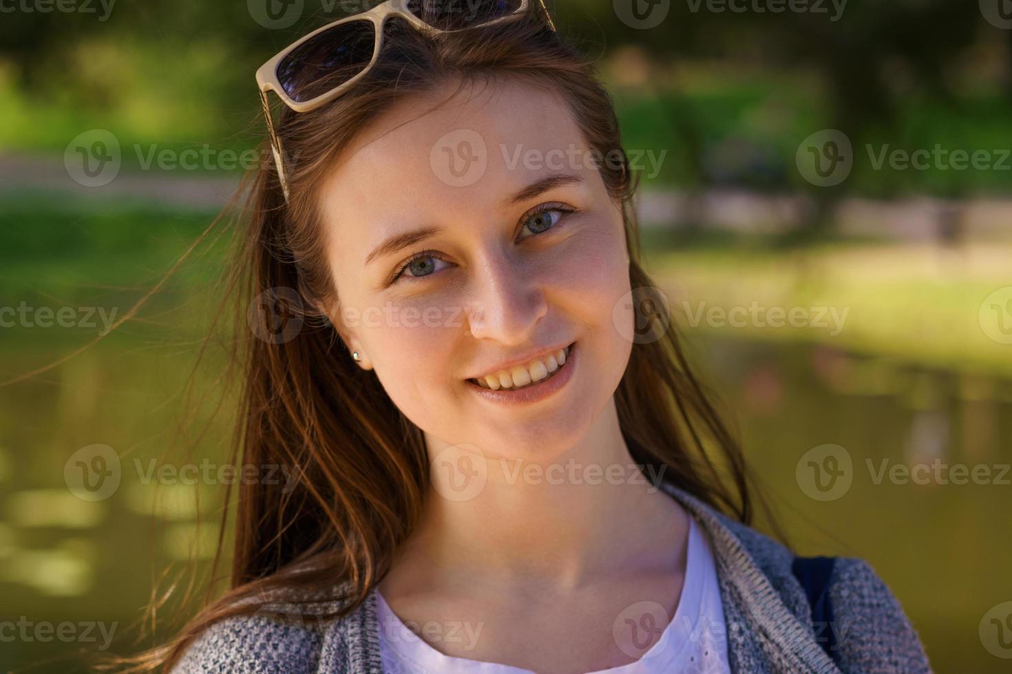 a woman in sunglasses smiles at the camera against the backdrop of a lake photo