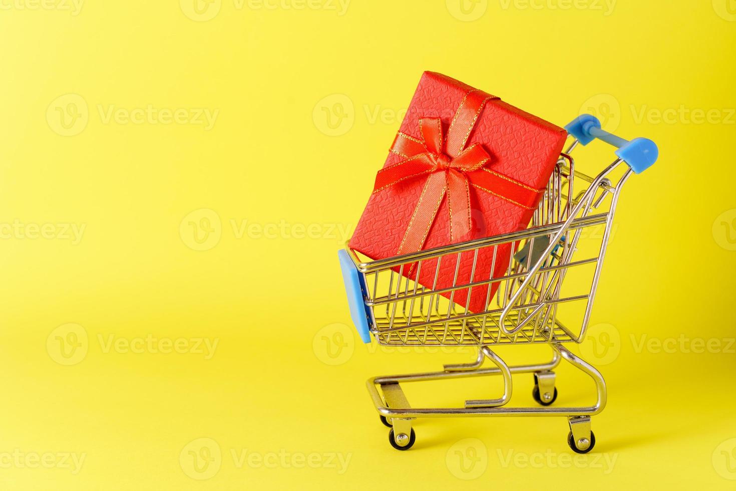 mini carrito con una pequeña caja de regalo roja sobre fondo amarillo. concepto de compras foto