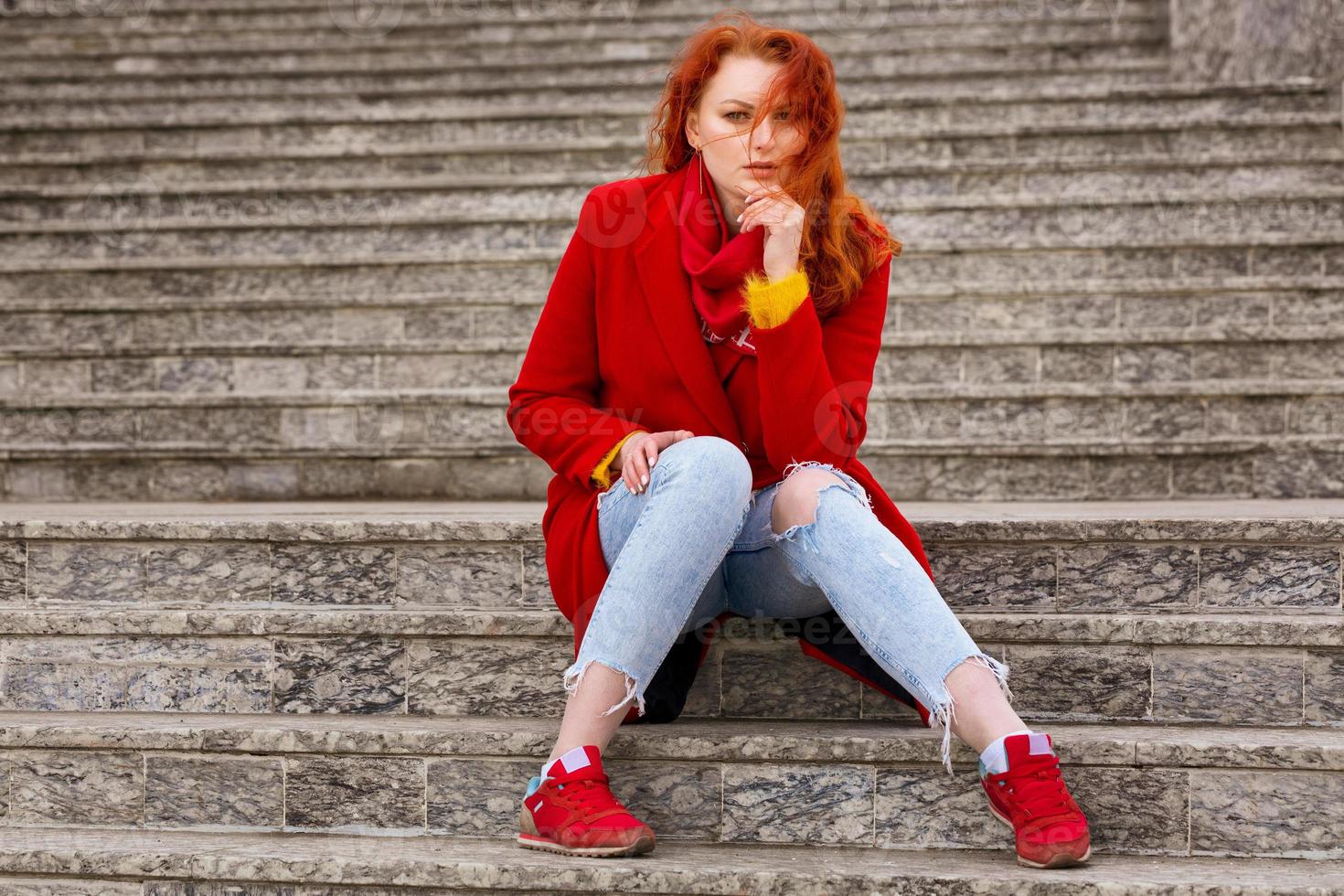 con pelo rojo en abrigo rojo y jeans está sentada en la calle en los escalones 5753577 Foto de en Vecteezy