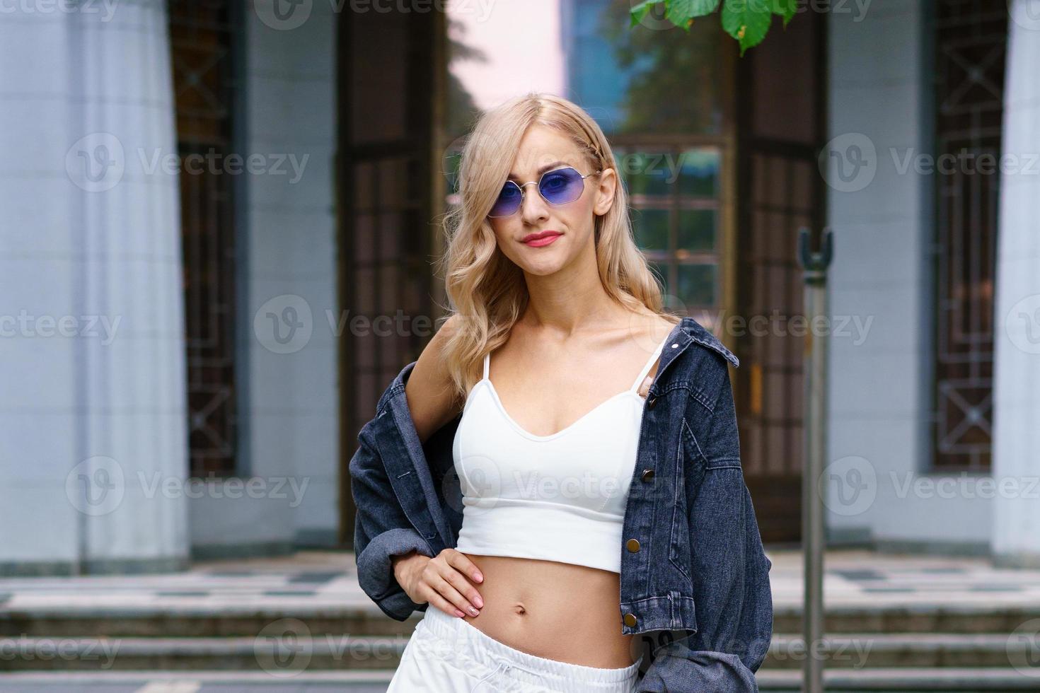 Young woman posing on the street of the city in a tracksuit and sunglasses photo