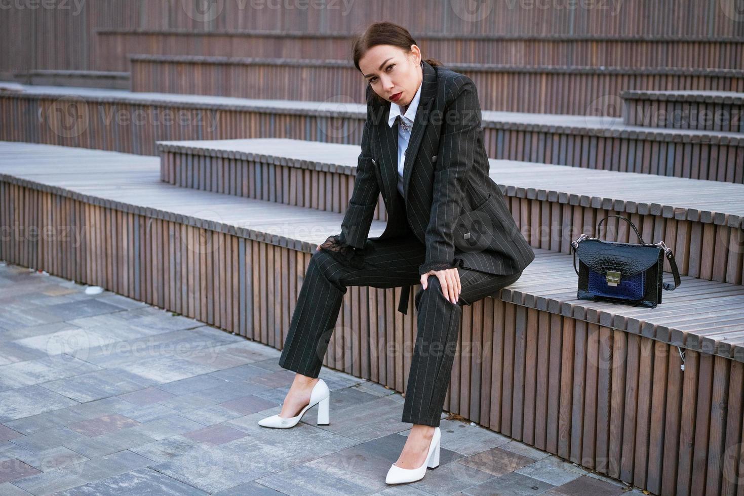 Business woman sitting on a bench in a suit and bag photo