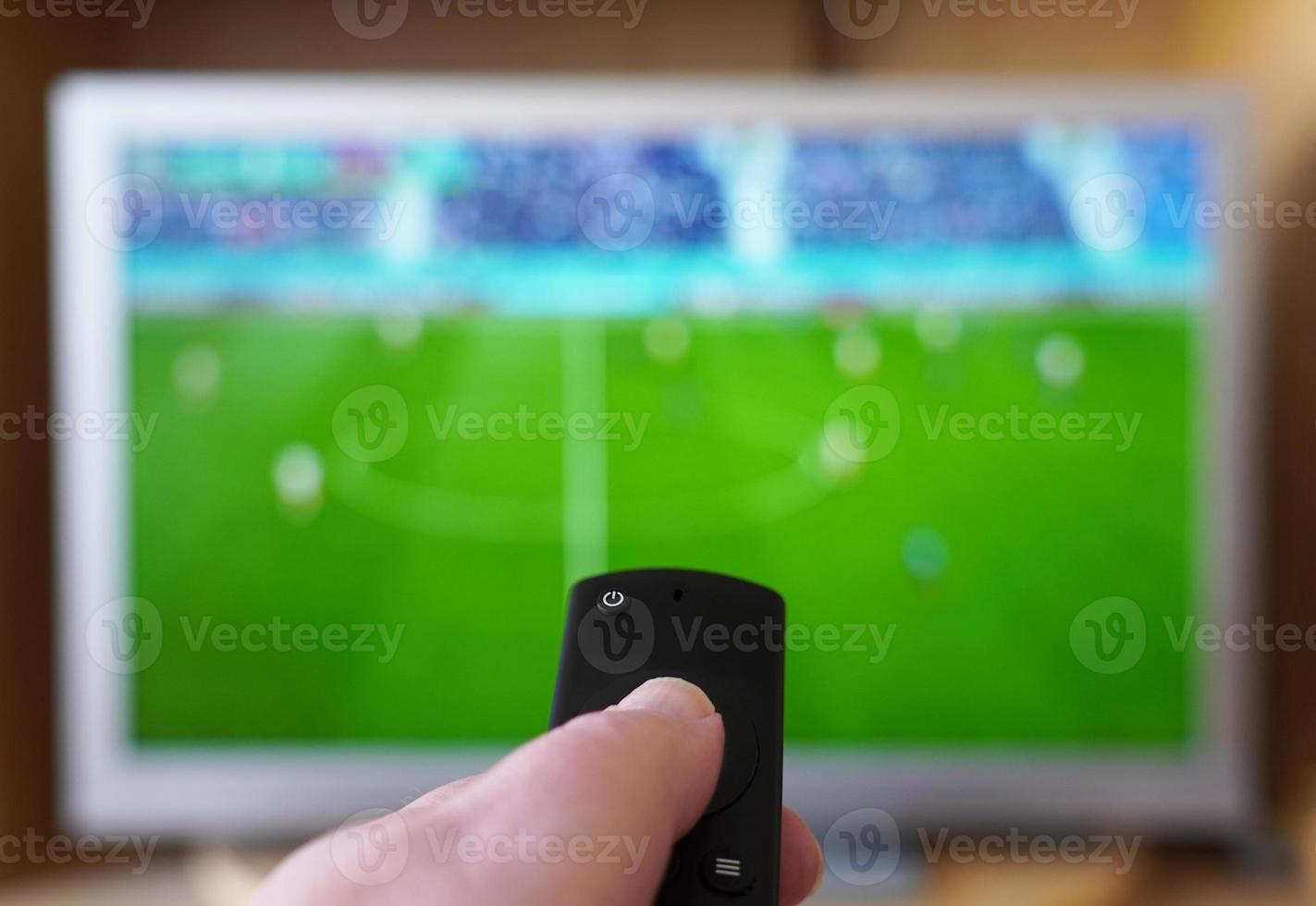 hand pointing remote control at tv with soccer or football match photo