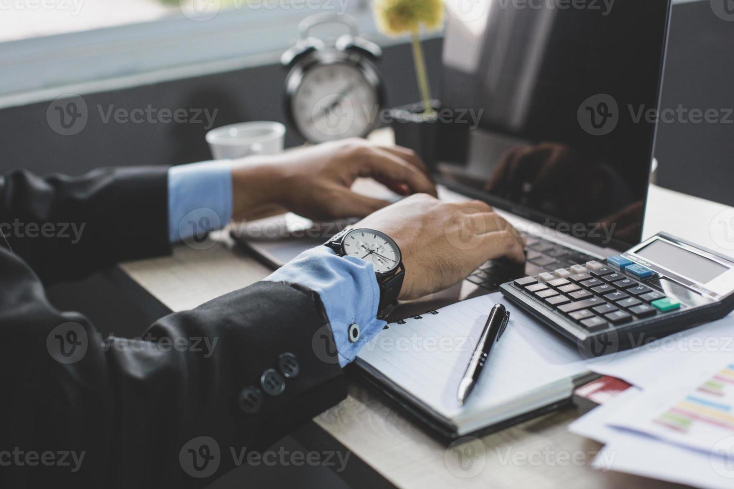 Businessman hands typing keyboard on a laptop with blurry background on office desk photo