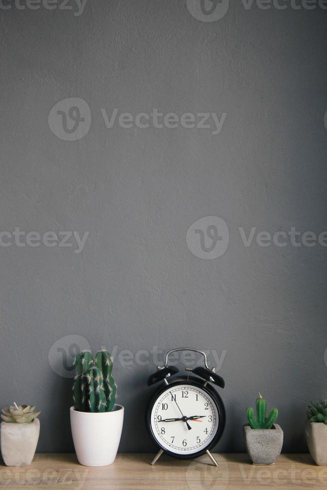 Alarm clock with succulents and cactus plants in pots on wooden table with grey background. Potted indoor house plants. Modern minimalist interior. photo