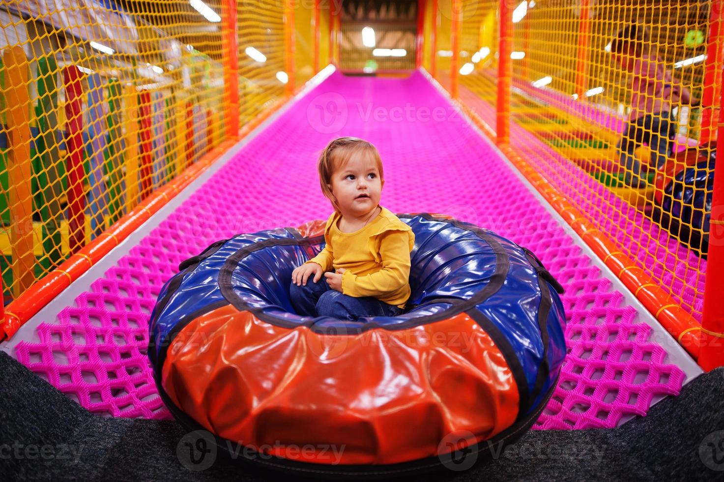 Baby girl sitting in tubing donuts enjoying slides in fun children center. photo