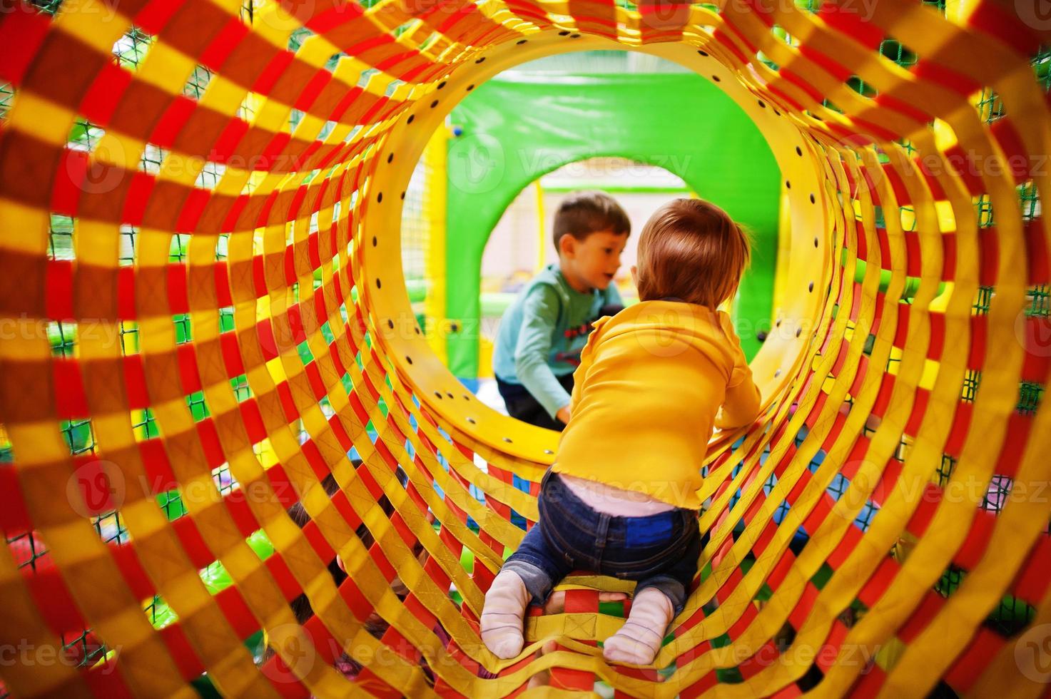 Kids playing in indoor play center. Kindergarten or preschool play room.  Baby girl climbs into the pipe. photo