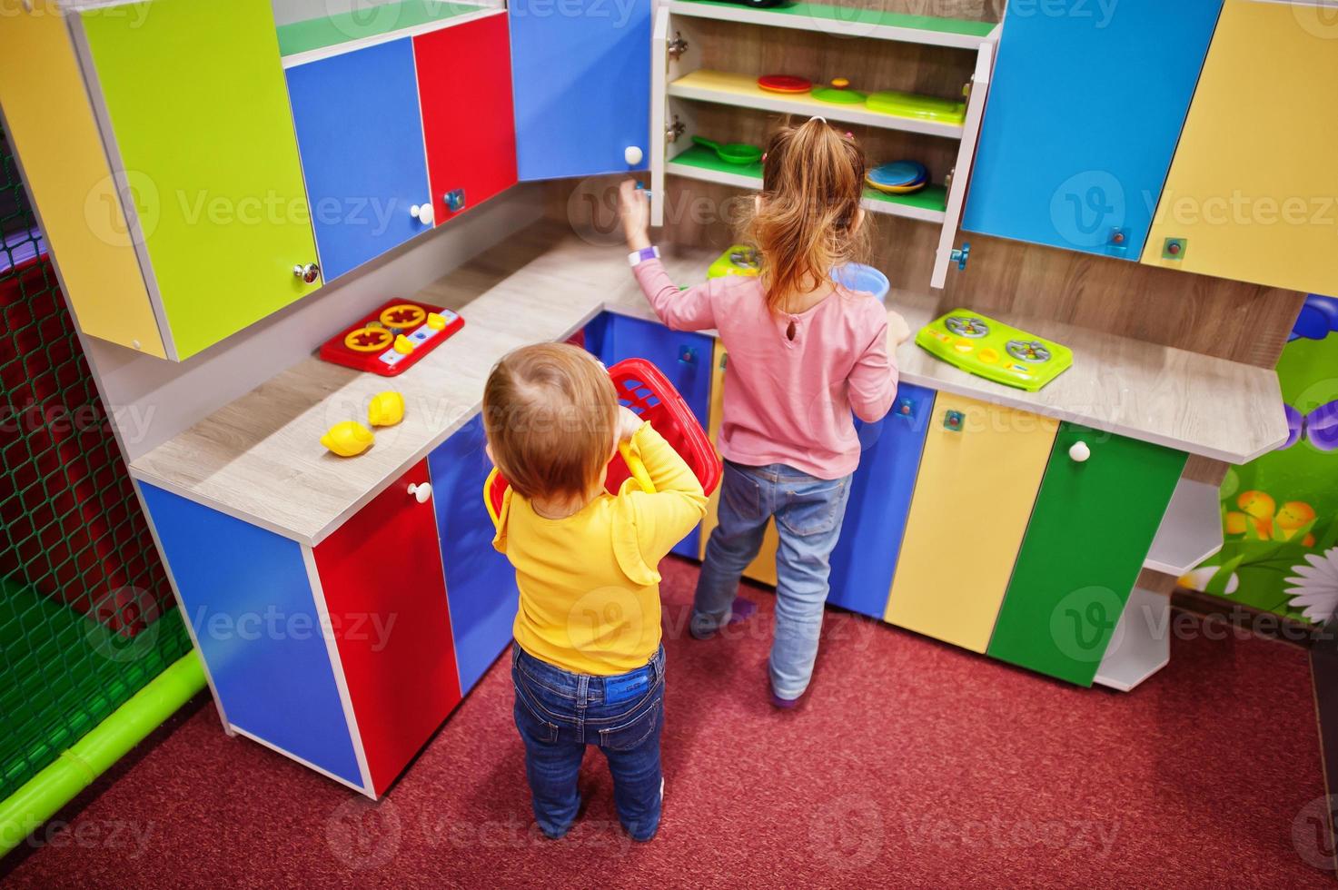 Cute sisters playing in indoor play center. Kindergarten or preschool play room. In the children's kitchen. photo