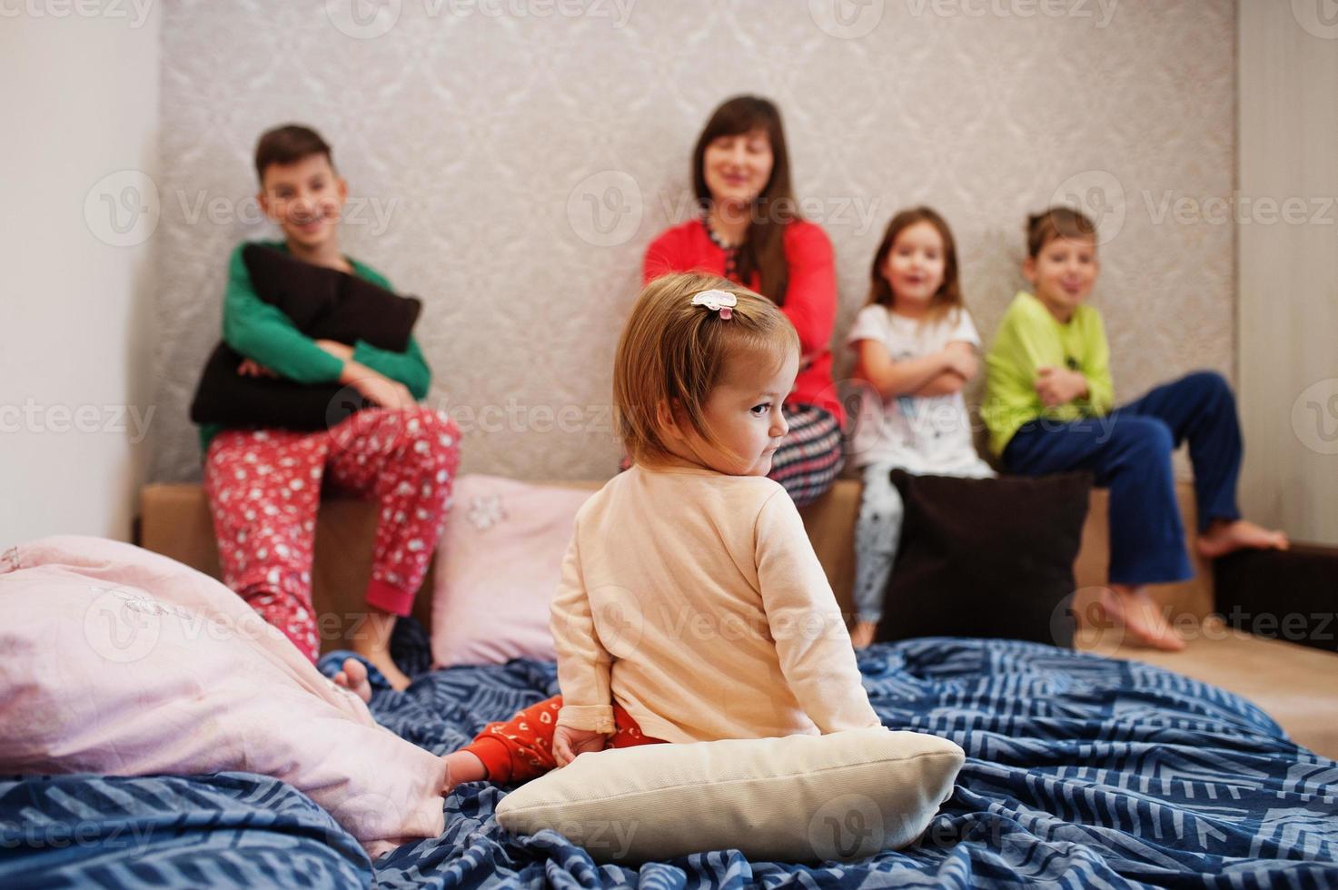 la gran familia feliz se está divirtiendo juntos en el dormitorio. gran concepto de mañana familiar. madre con cuatro hijos usa pijama en la cama en casa. foto