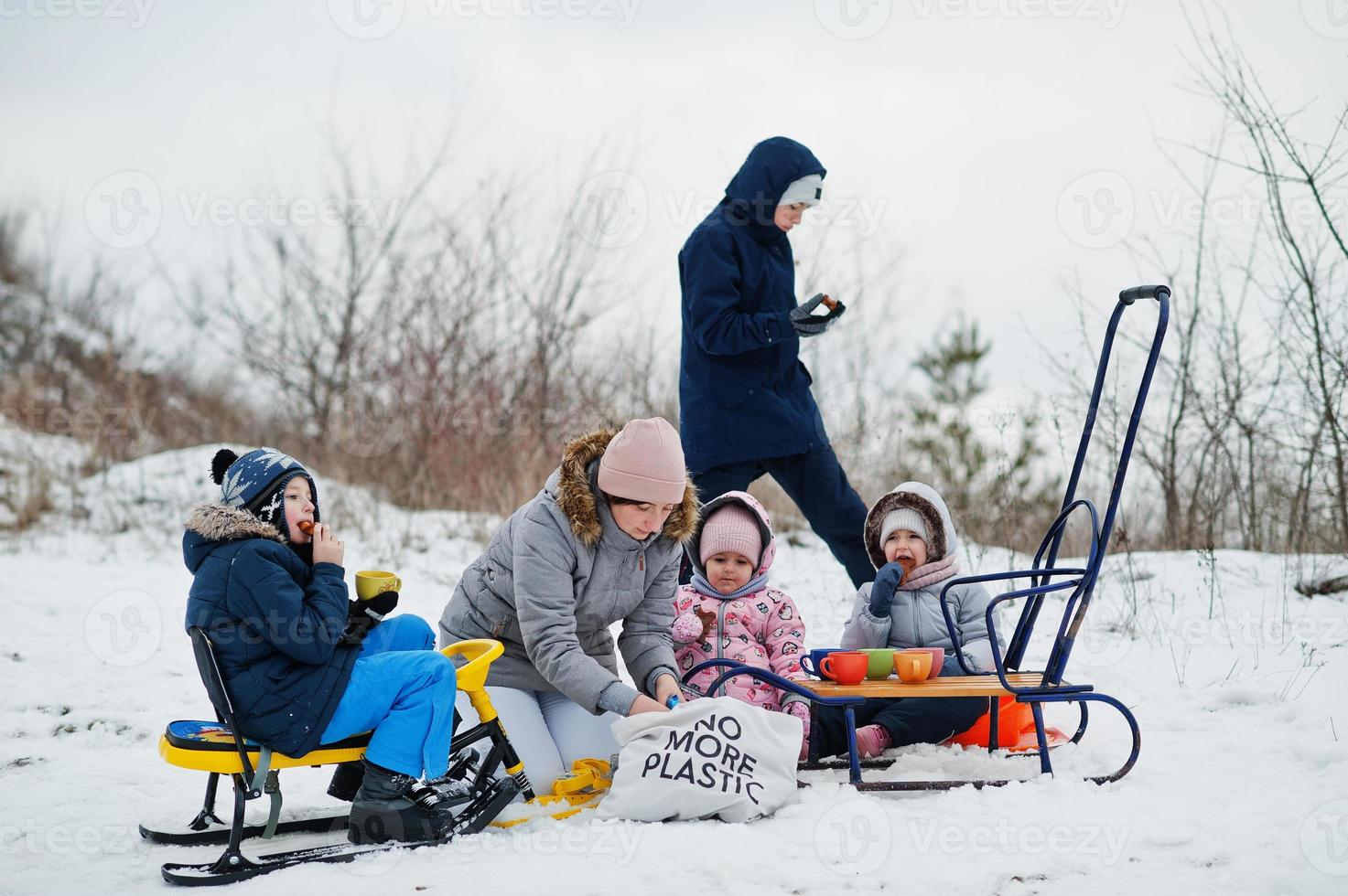 Family plays and sleigh rides in winter outdoor, children having fun, drinking tea. photo