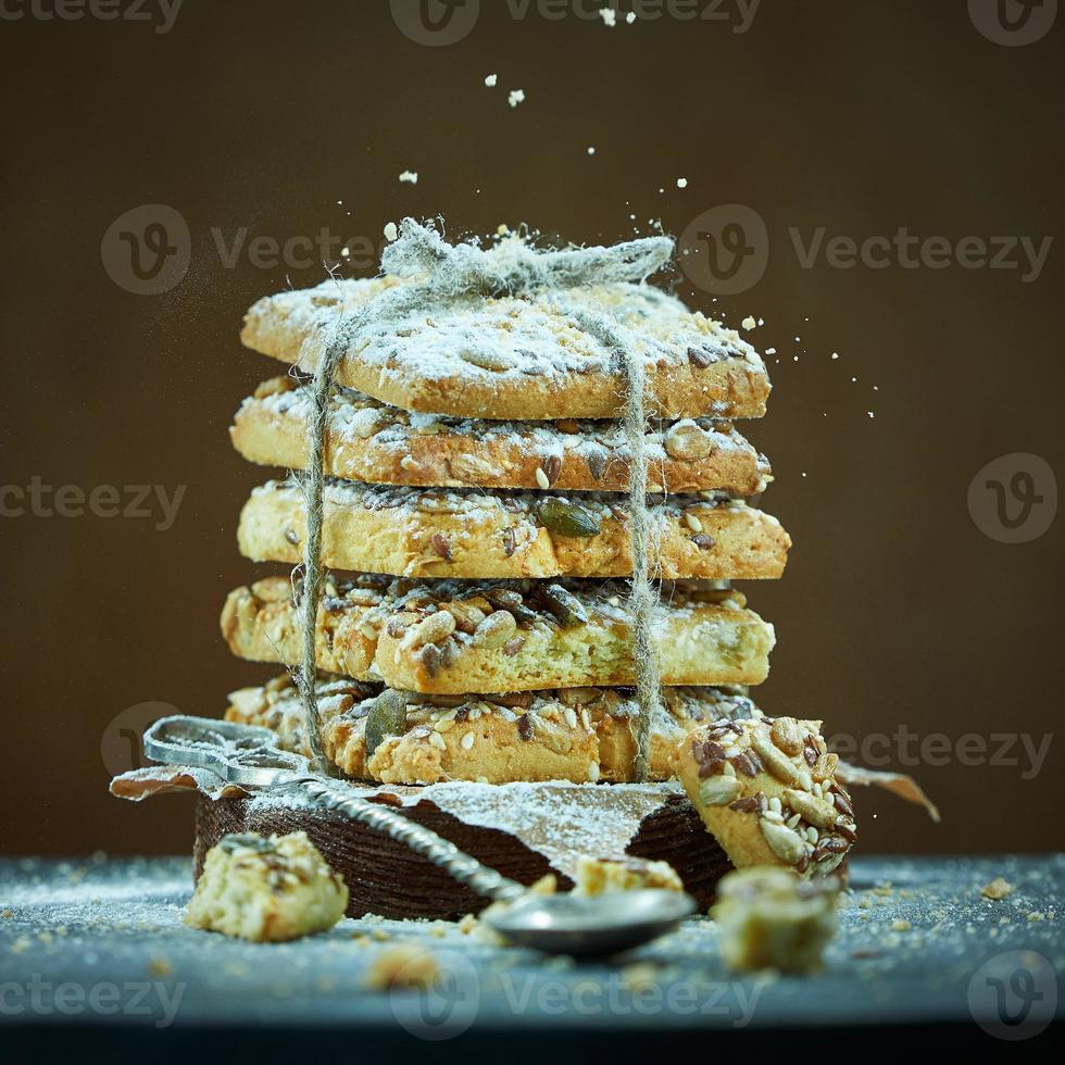 Square cookies with nuts and seeds tied with rope are sprinkled with powdered sugar on a brown background. Foreground of spoon and cookie crumbs in a blur. photo