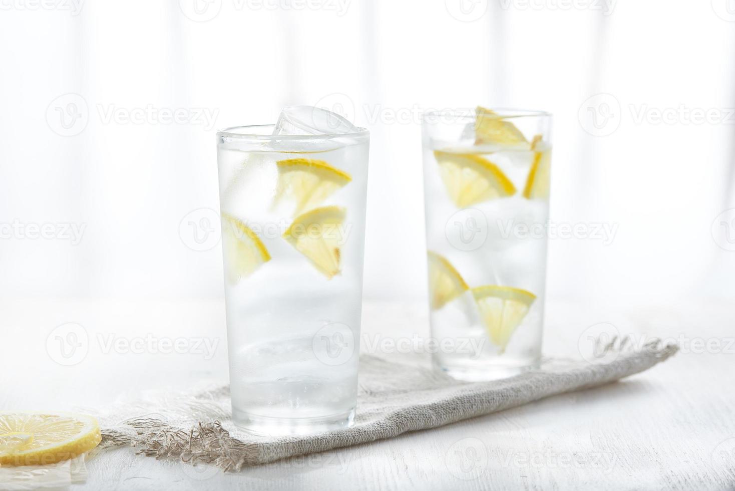 Two glasses of ice cold lemonade with lemon slices on linen napkin on white background in blur. photo