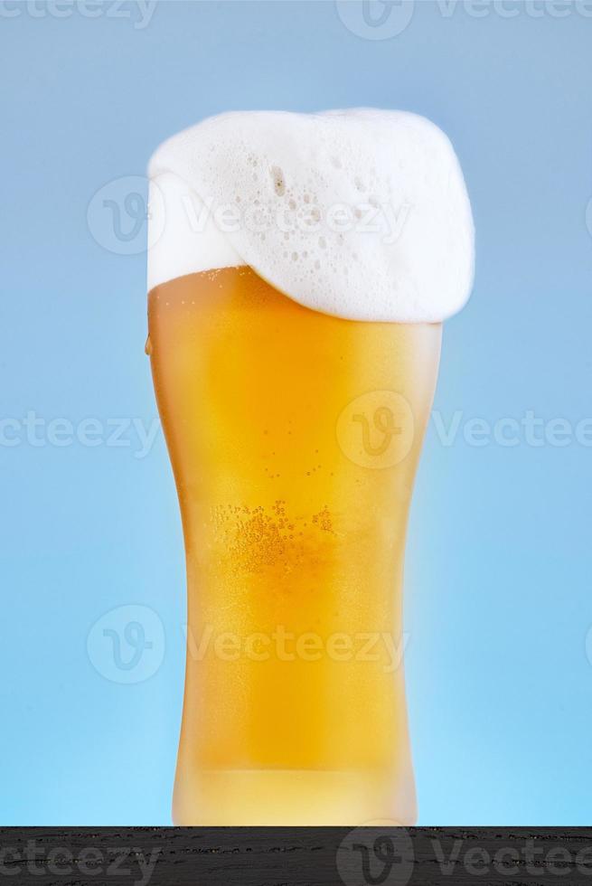 Beer glass close-up on a blue background. Foam spills over the edge. photo