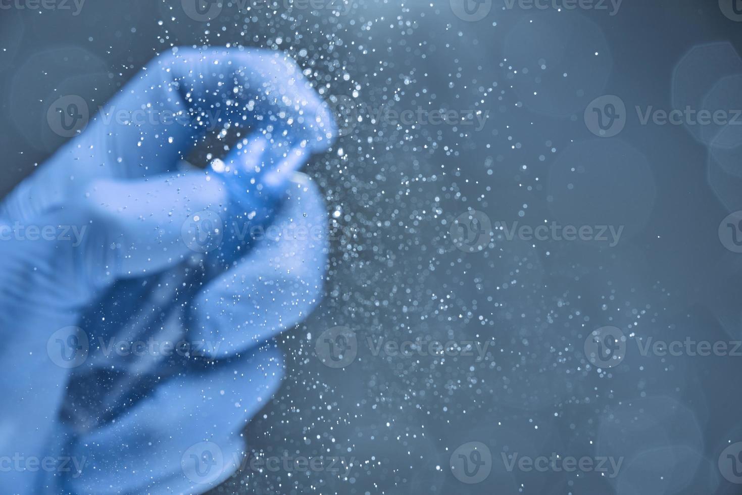 A hand in a rubber glove in a blur sprays the glass with a sanitizer. photo