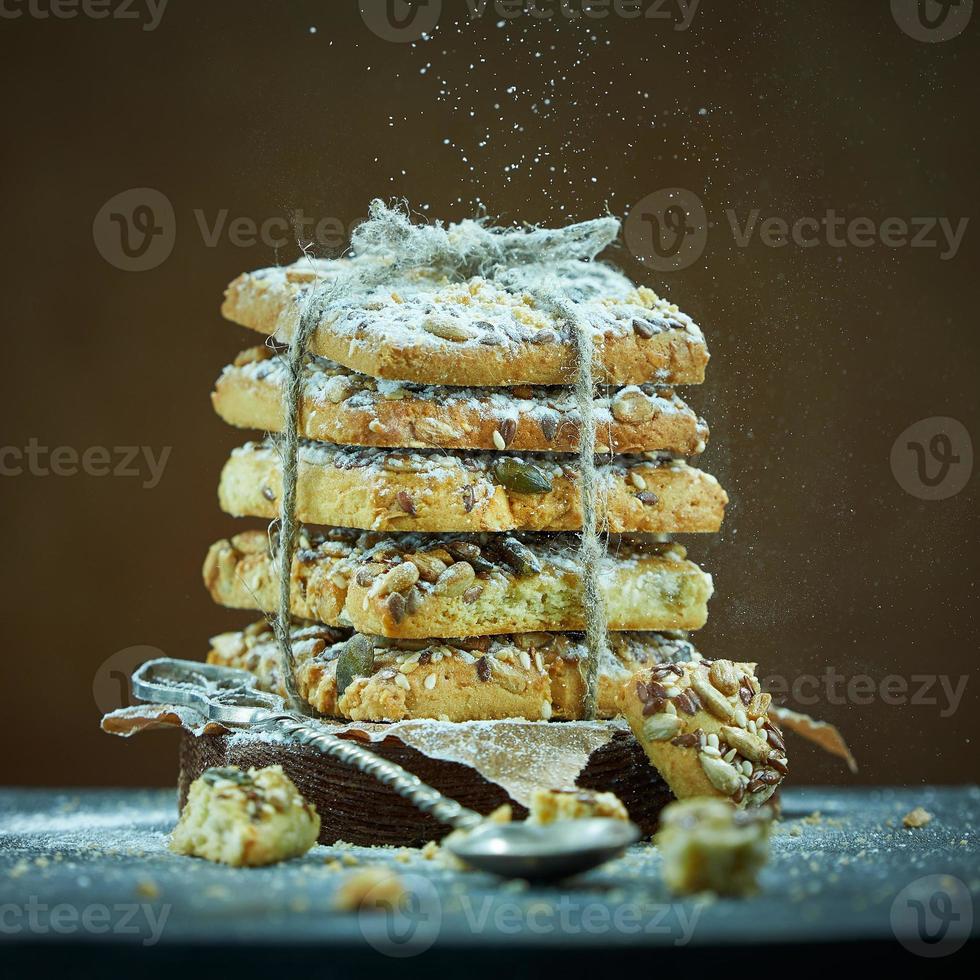 Square cookies with nuts and seeds tied with rope are sprinkled with powdered sugar on a brown background. Foreground of spoon and cookie crumbs in a blur. photo