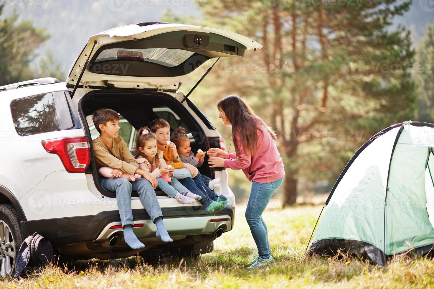 Family of four kids and mother at vehicle interior. Children sitting in trunk. Traveling by car in the mountains, atmosphere concept. photo