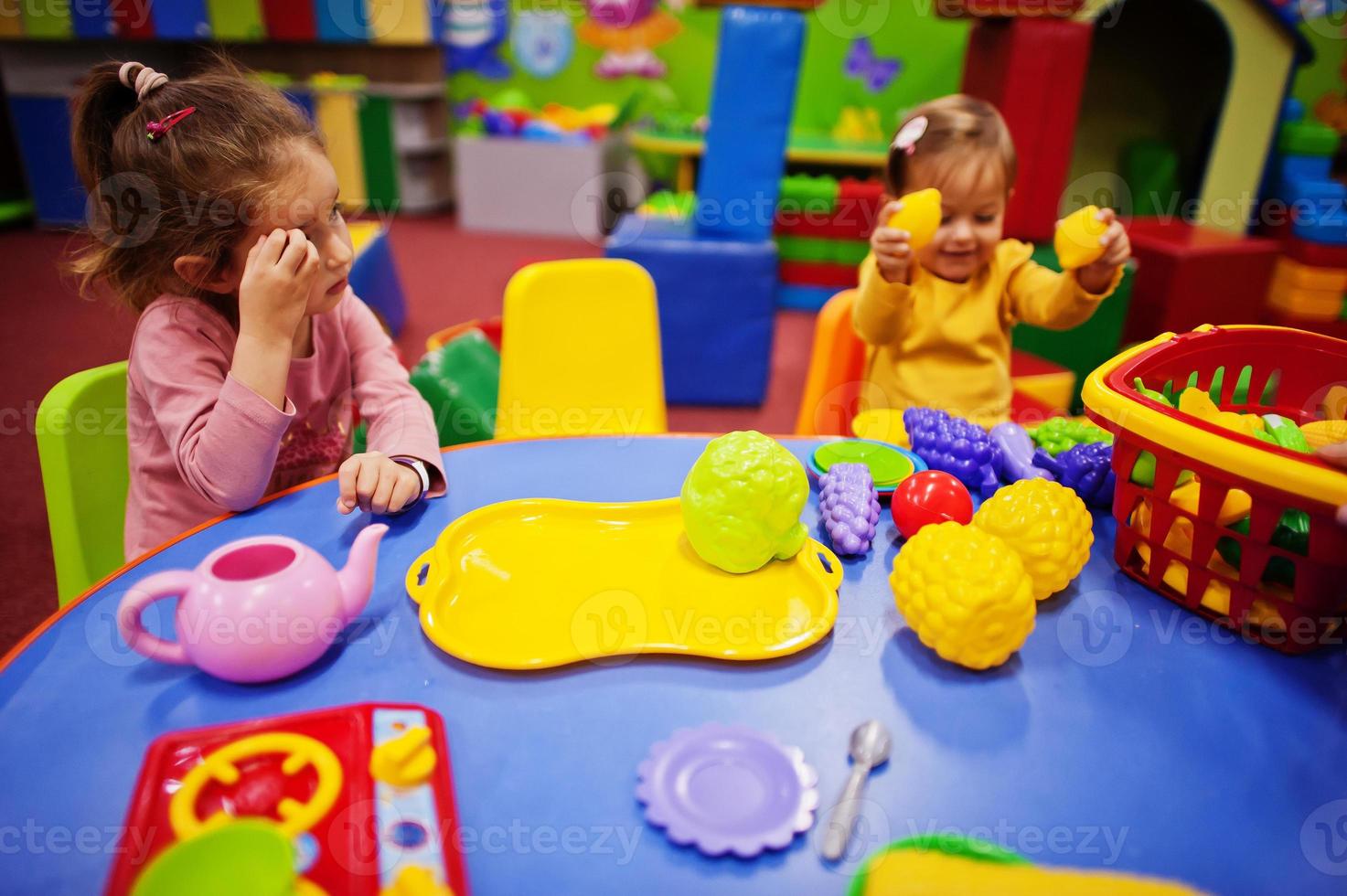 Cute sisters playing in indoor play center. Kindergarten or preschool play room. In the children's kitchen. photo