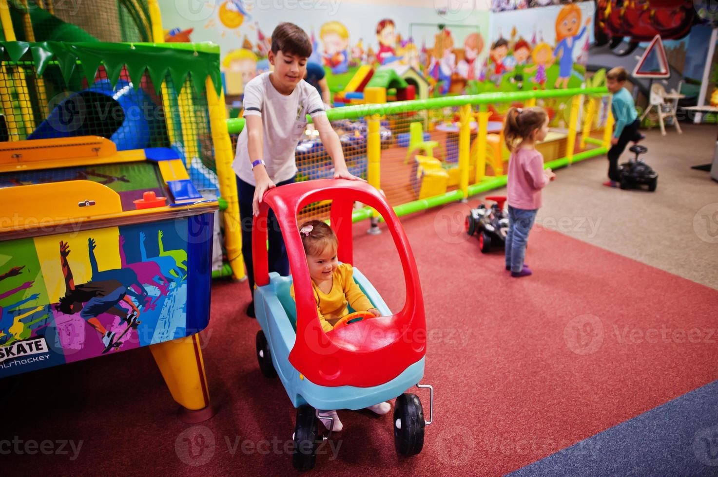 cuatro niños jugando en el centro de juegos interior. sala de juegos de jardín de infantes o preescolar. montar coche de juguete. foto