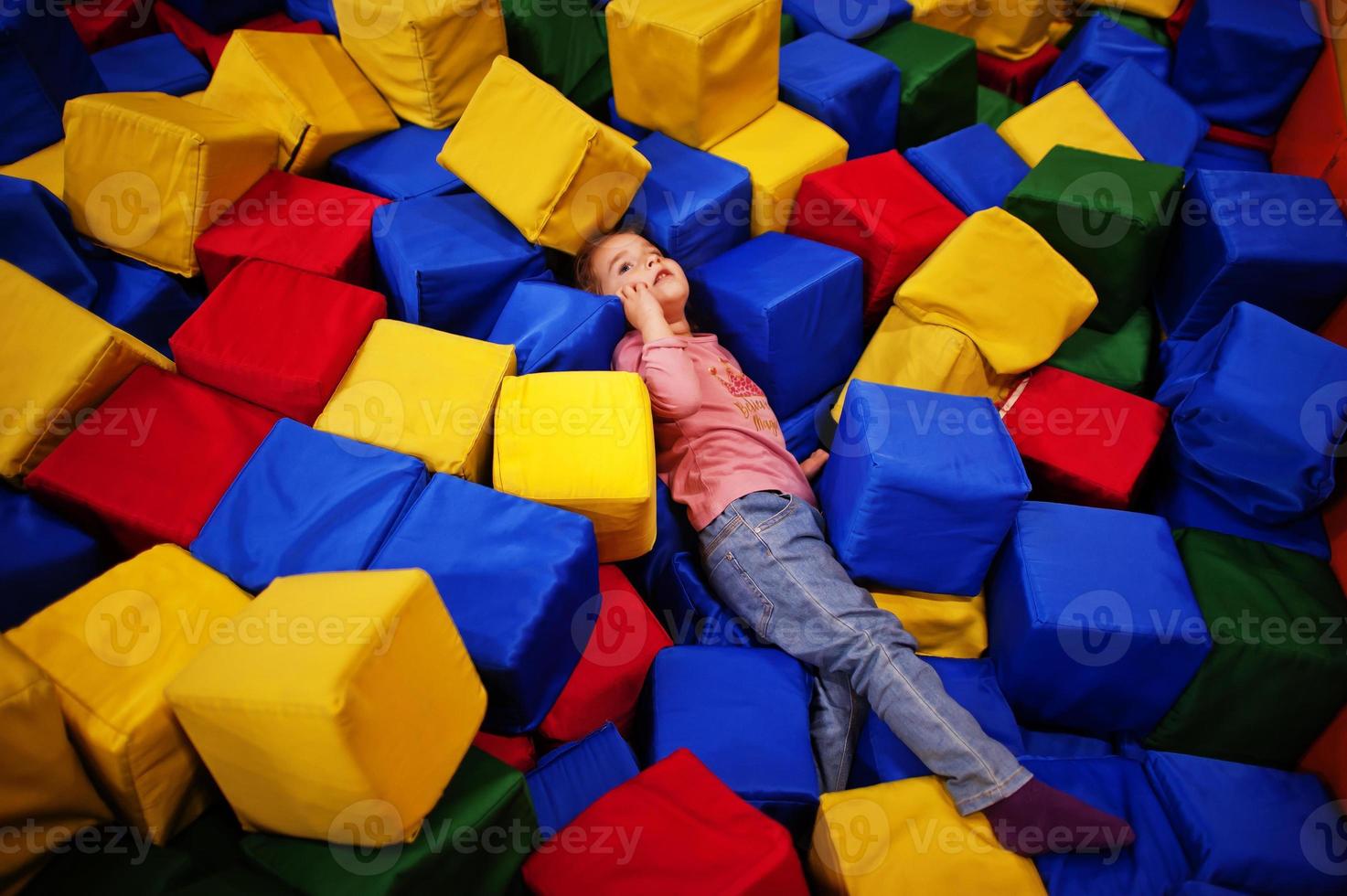 linda niña tendida en la piscina con cubos de espuma de colores en el centro de juegos interior. foto