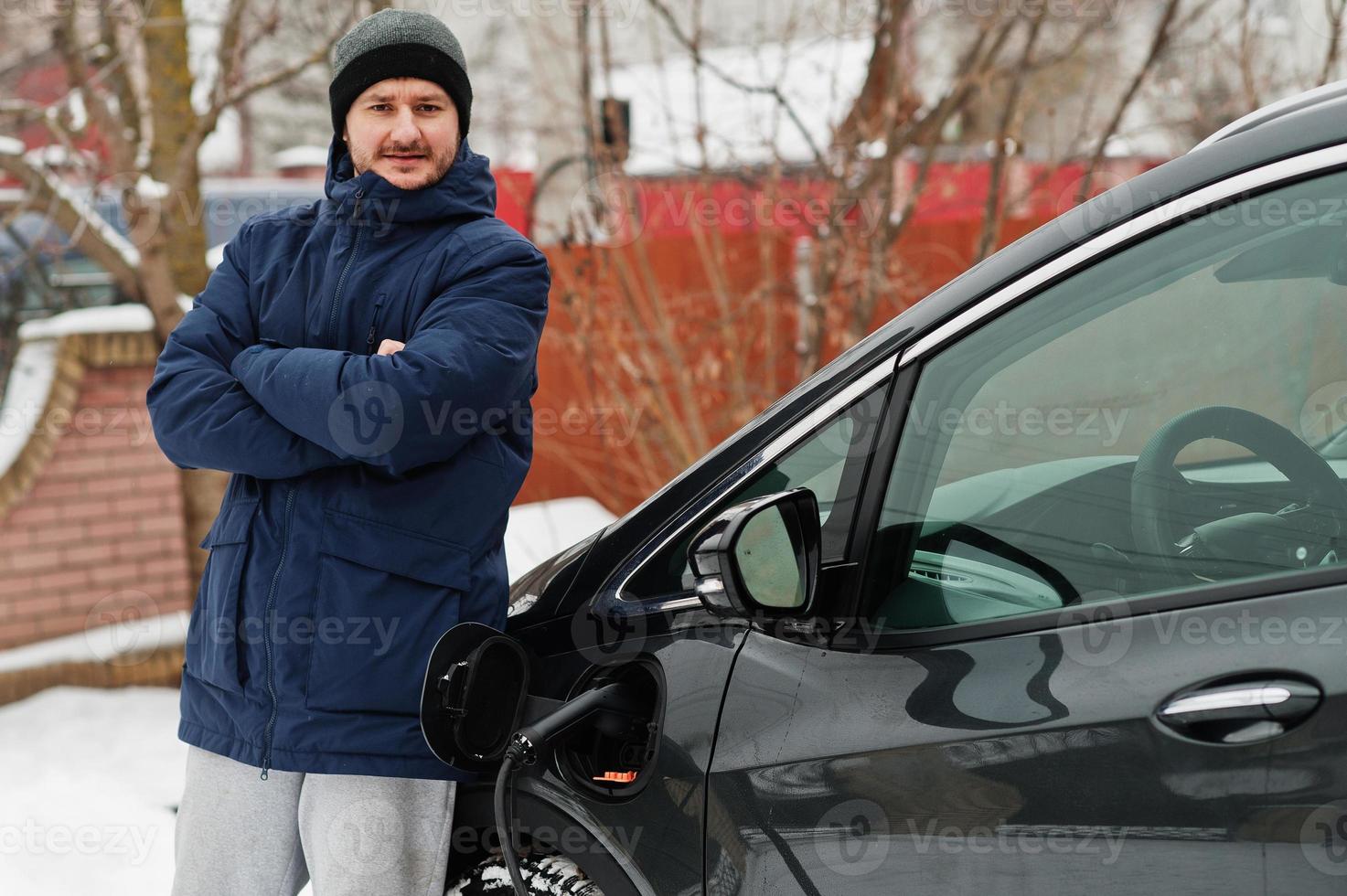 Young man charging his electric car in winter. Eco transport concept. photo
