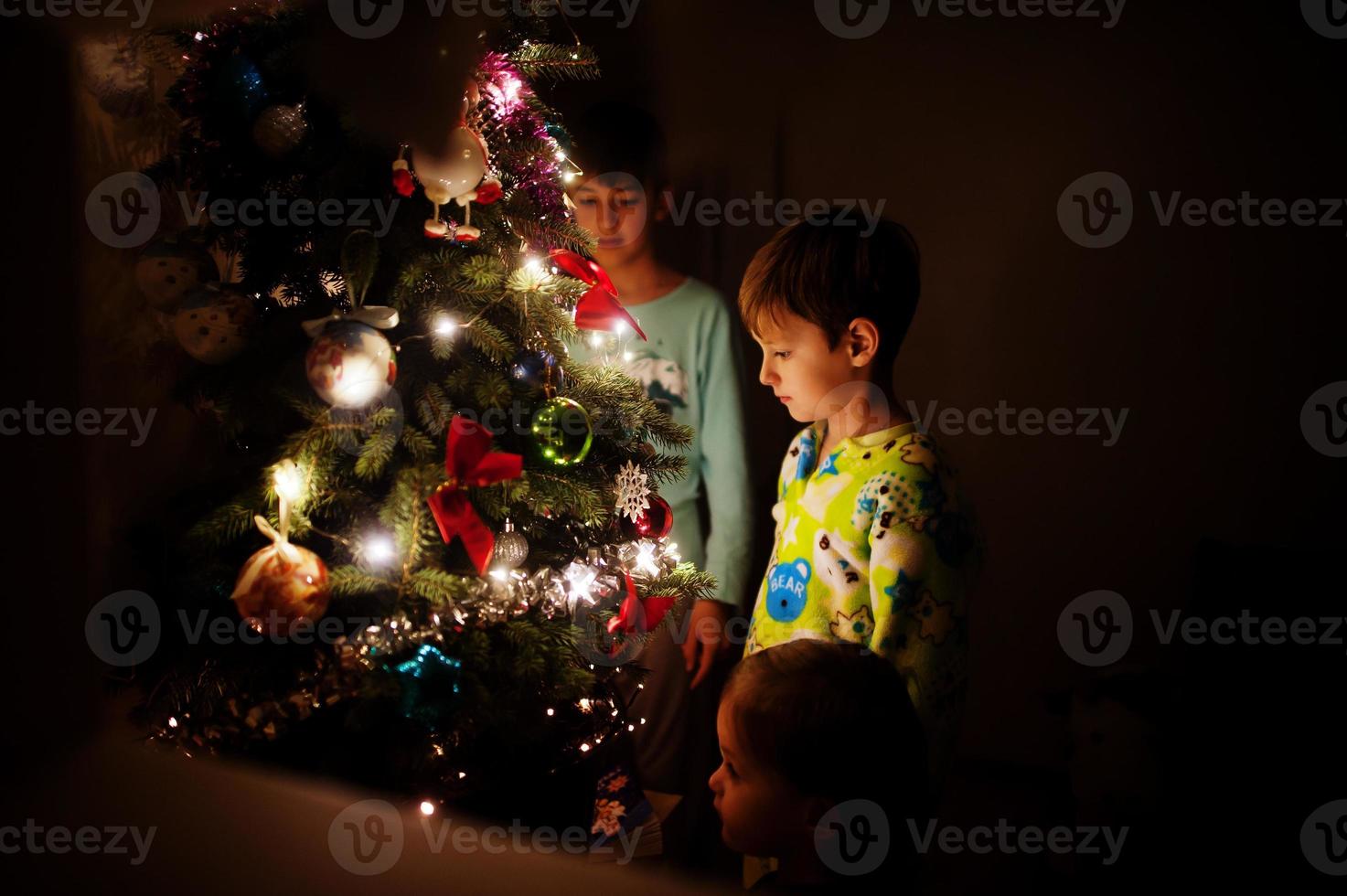 Kids looking on Christmas tree with shining garlands on evening home. photo