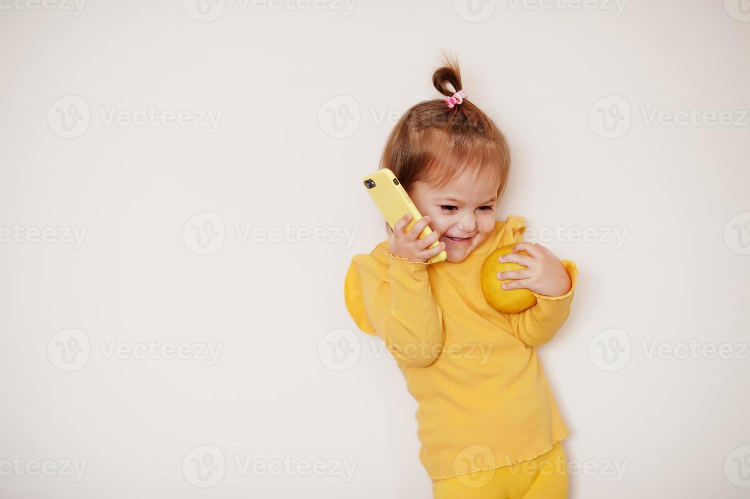 Baby girl in yellow with lemon and mobile phone, isolated background. photo
