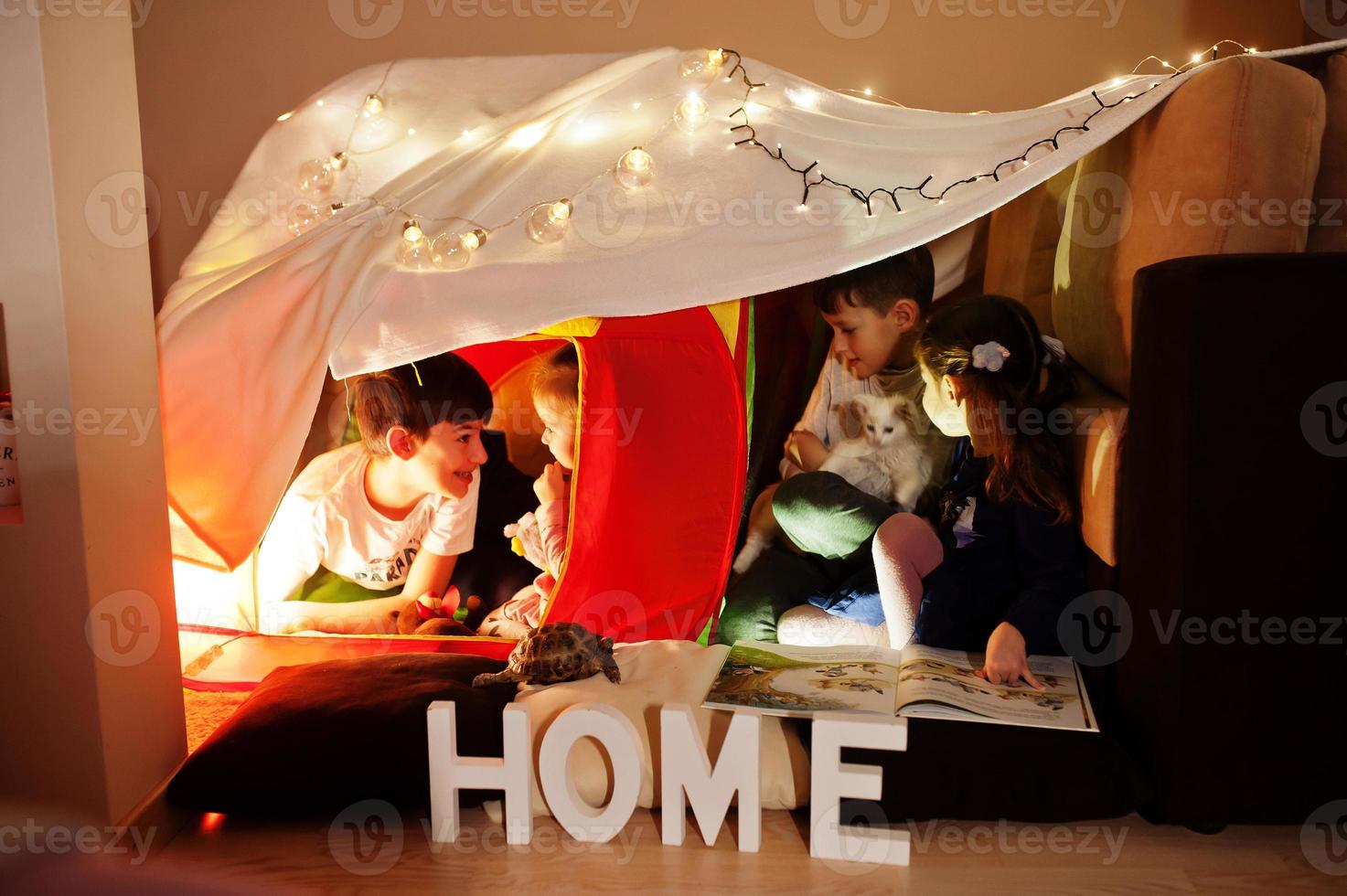 Playing kids with kitty in tent at night home. Hygge mood. photo