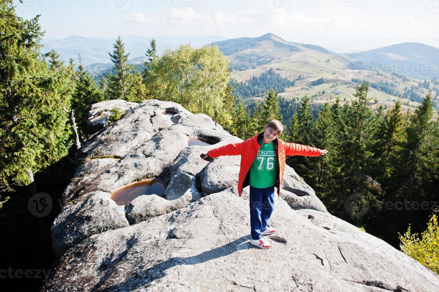 niño en la cima de la montaña. los niños caminan en un hermoso día en las montañas, descansan en la roca y admiran las increíbles vistas de los picos. vacaciones familiares activas con niños. diversión al aire libre y actividad saludable. foto