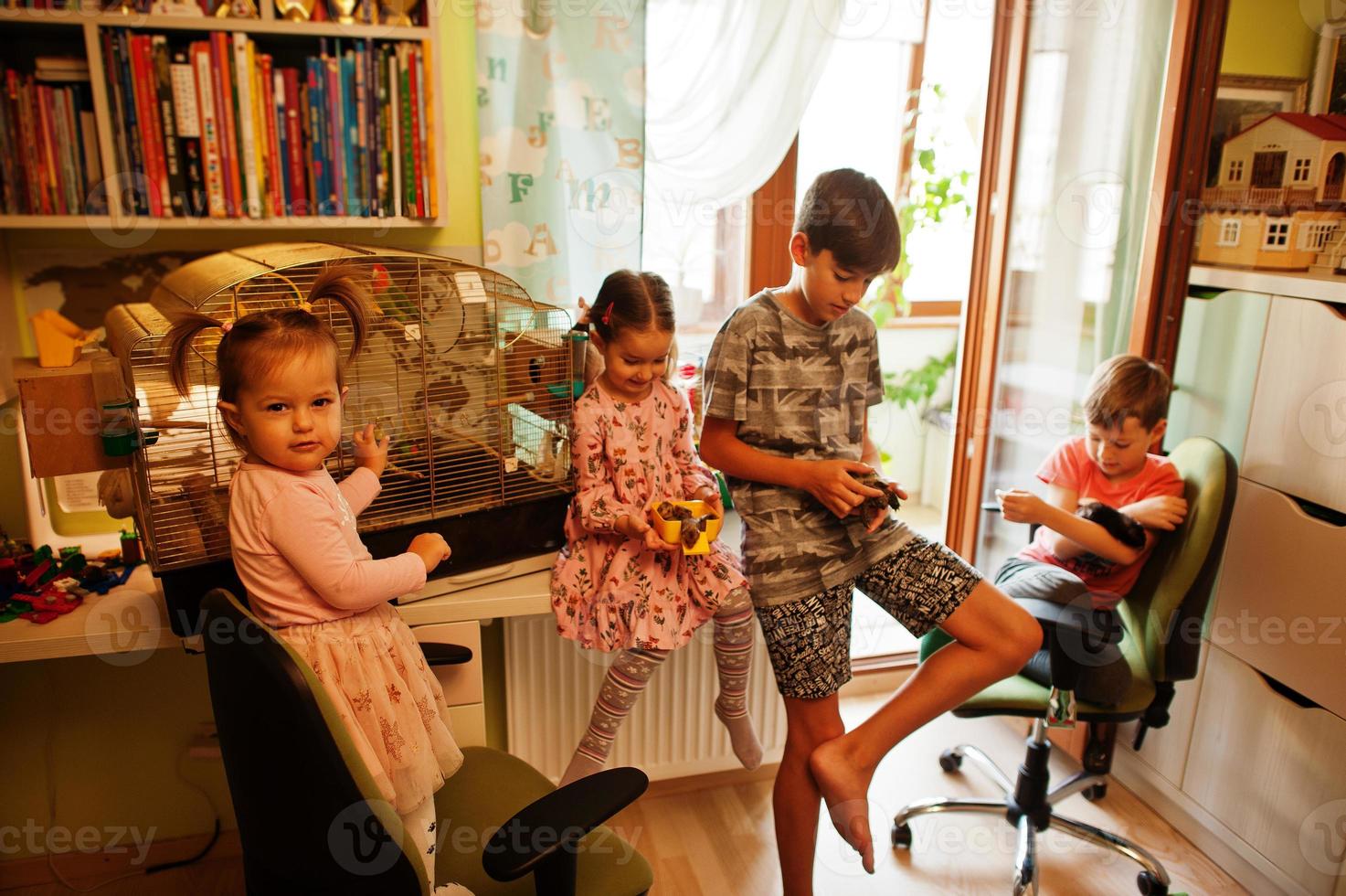 Four children holding their favorite pets on hands. Kids playing with hamster,turtle and parrots at home. photo