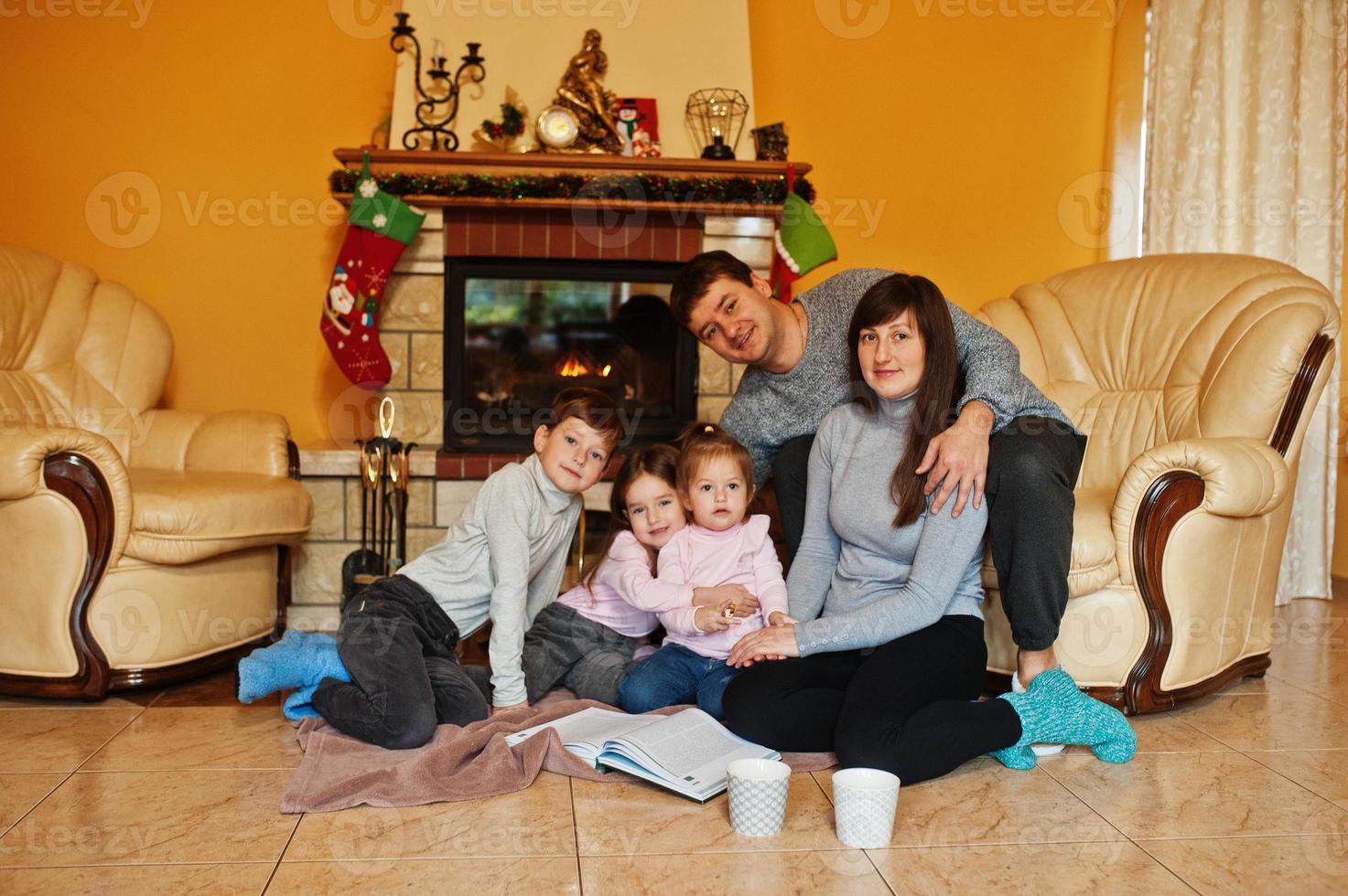 Happy young large family at home by a fireplace in warm living room on winter day. photo