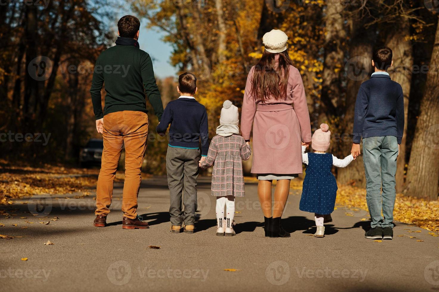 Large family with four kids holding hands and stand on road at autumn park, back view. photo