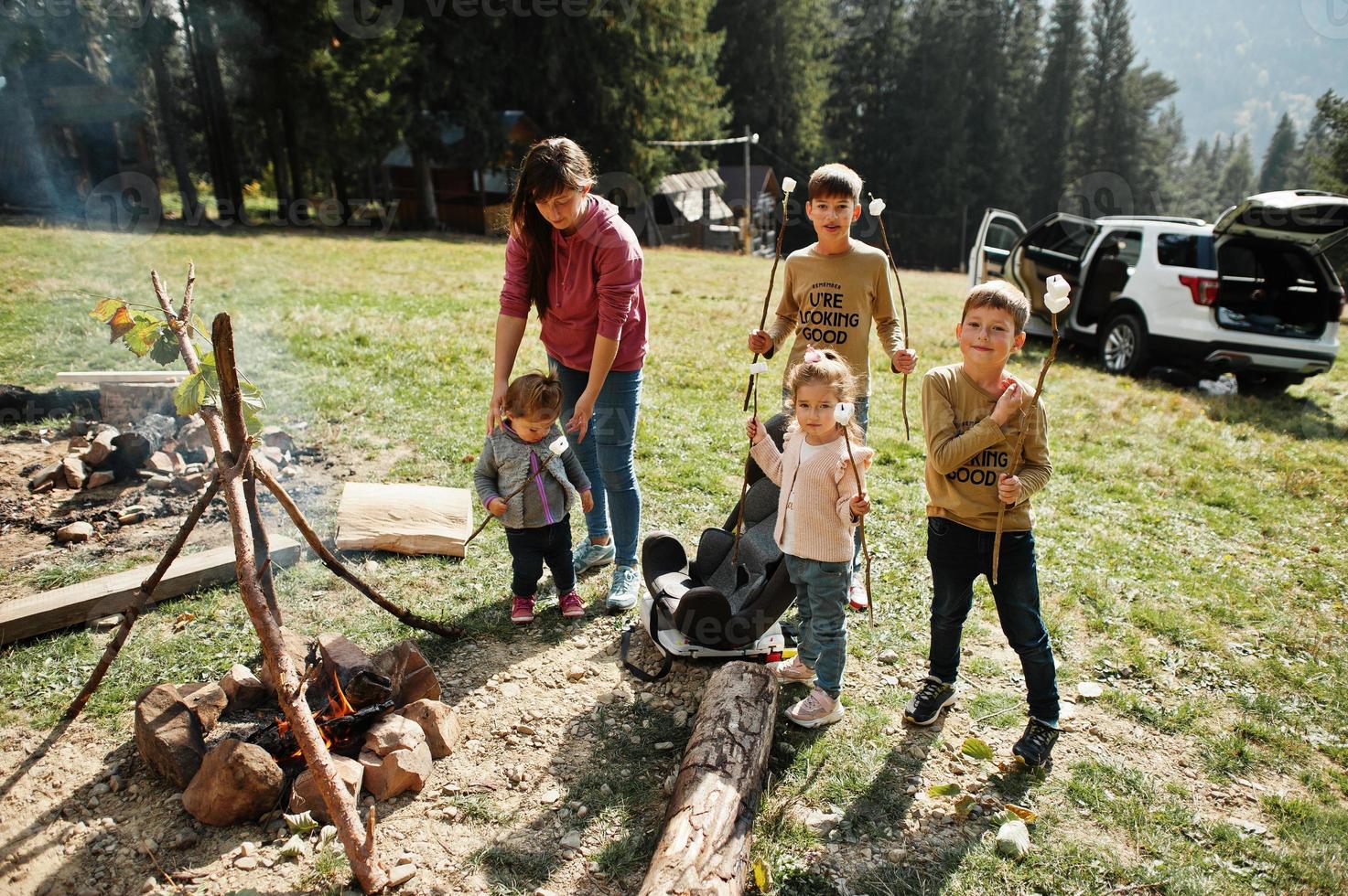 hoguera familiar en la montaña. cuatro niños acampando. malvaviscos a la barbacoa. Caminata de otoño y clima de campamento. calentar y cocinar cerca de la llama juntos. foto