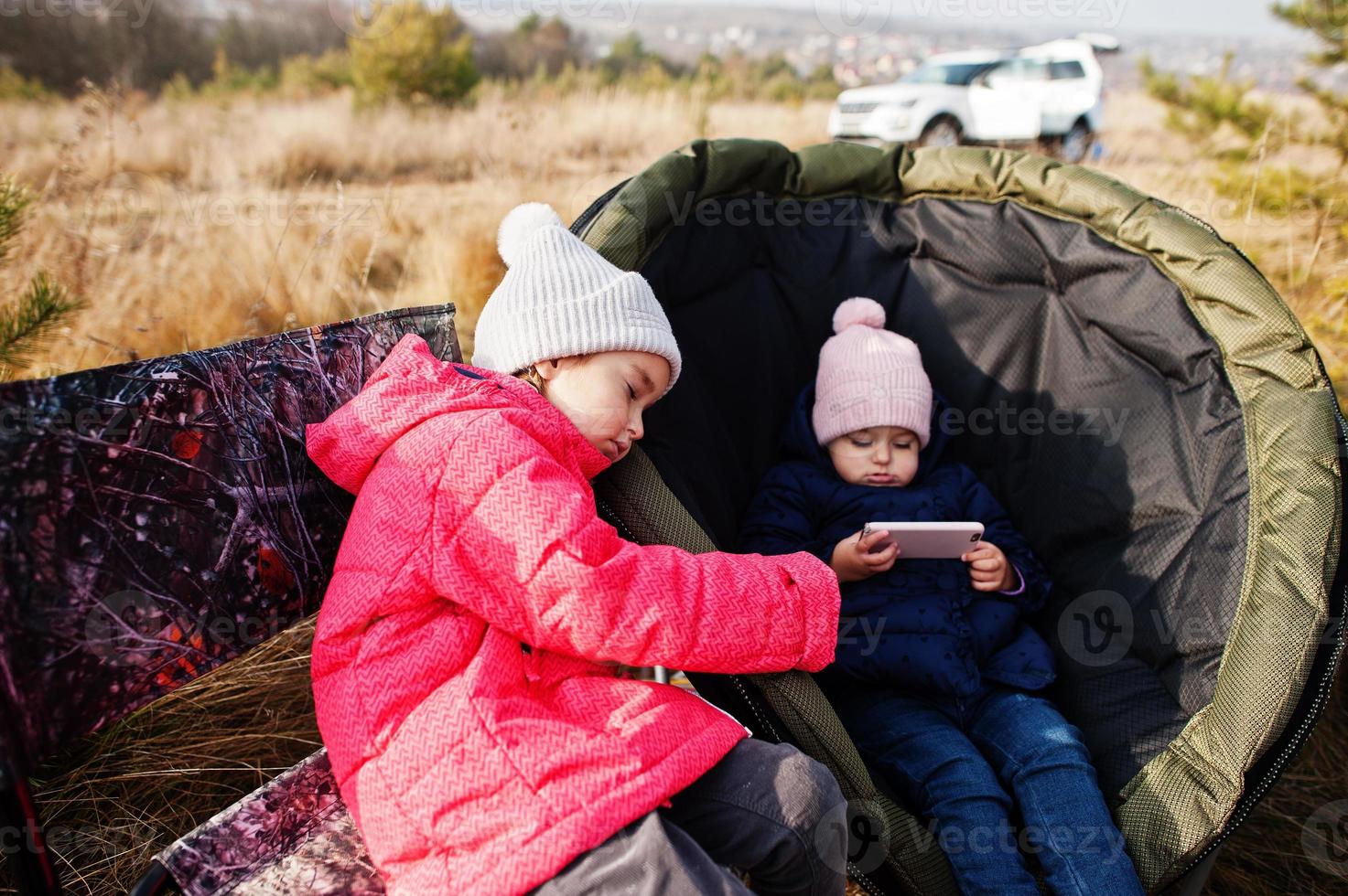 Two sisters sitting on chair outdoor picnic and watching cartooons on mobile phone. photo