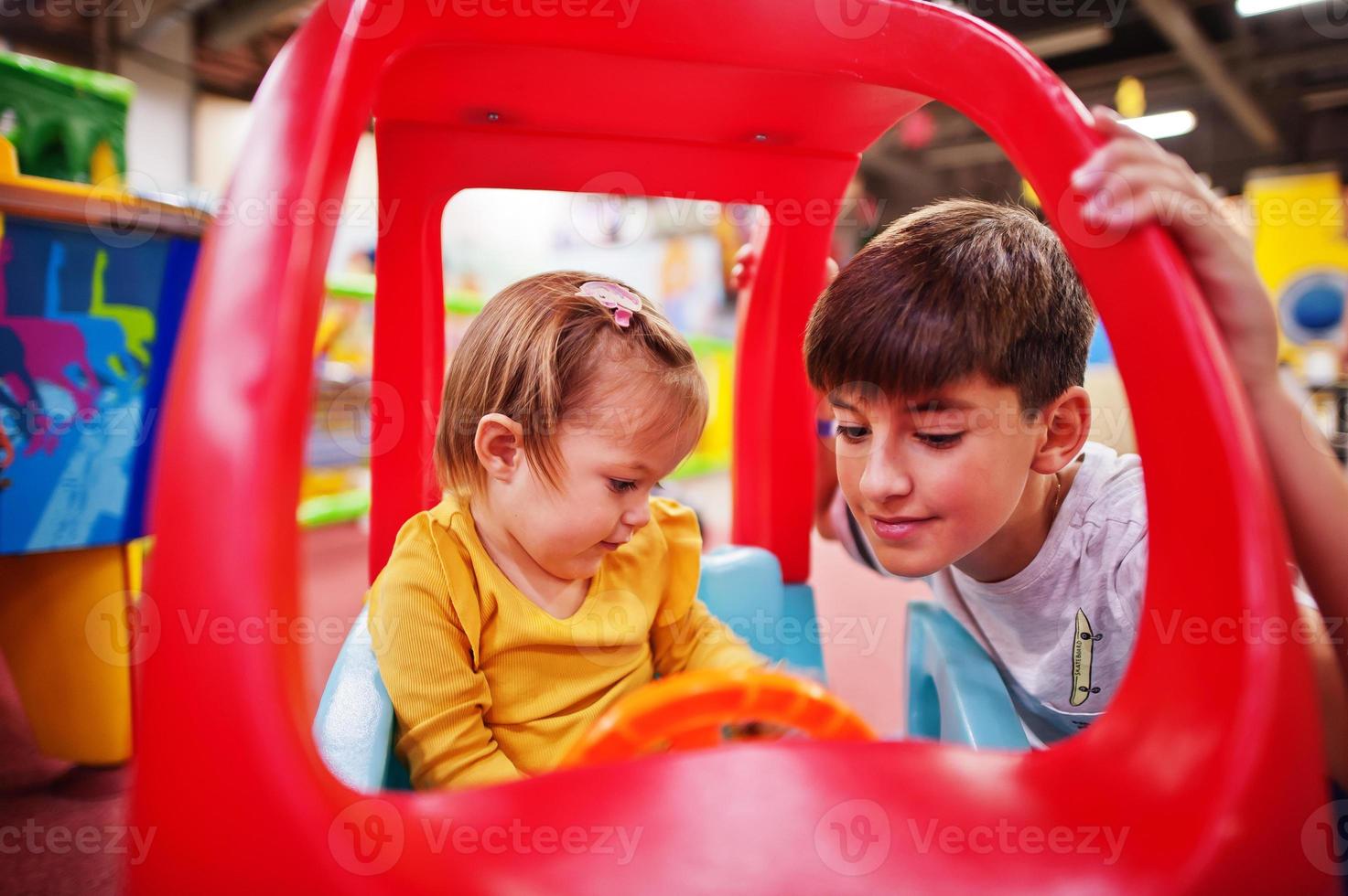 hermano con hermana monta en un coche de plástico en el centro de juegos interior. foto