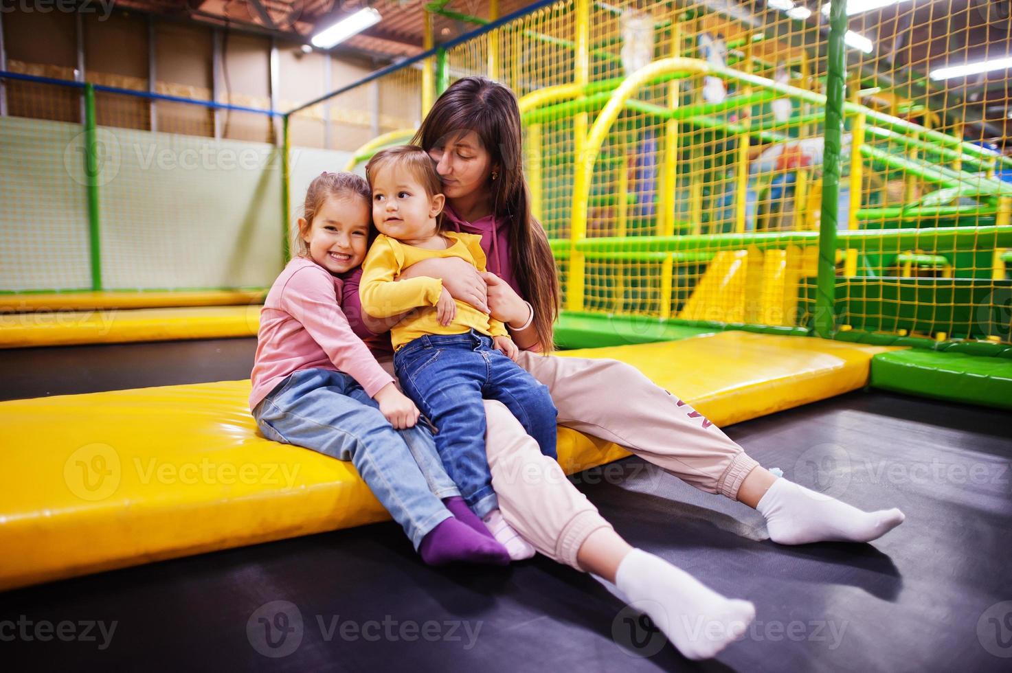 Mother with two daughters sitting on a trampoline in indoor play center. photo