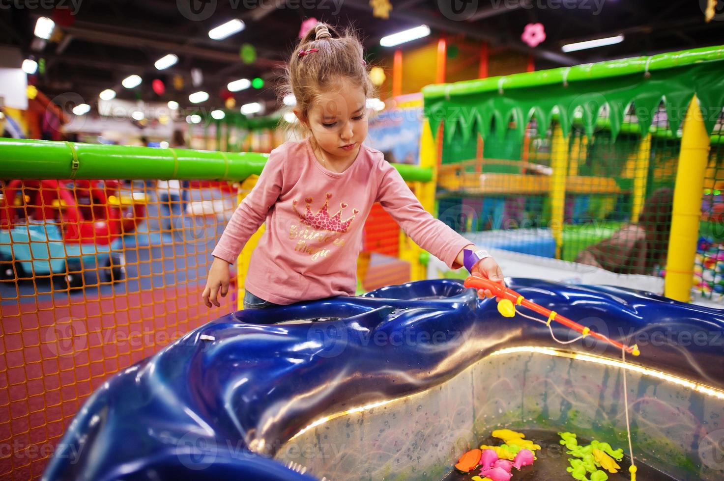 Cute baby girl playing in indoor play center. Kindergarten or preschool play room. Catches fish in the pool. photo