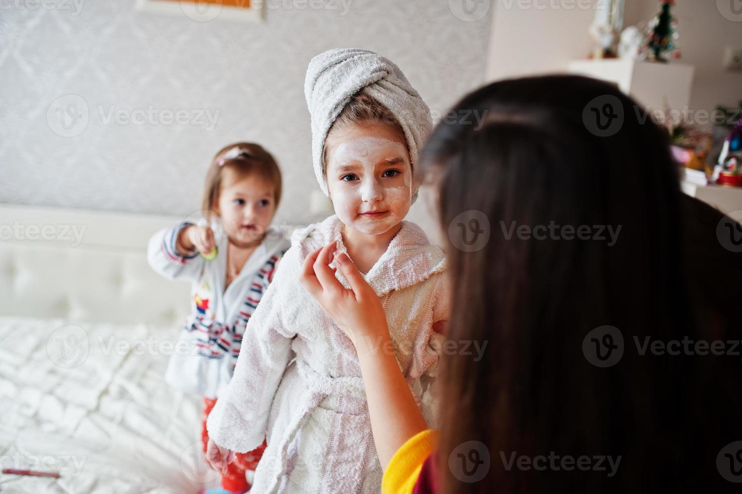 Mother with daughters in a bathrobe with a towel on her head take care of the skin at home, cucumbers on eyes. photo