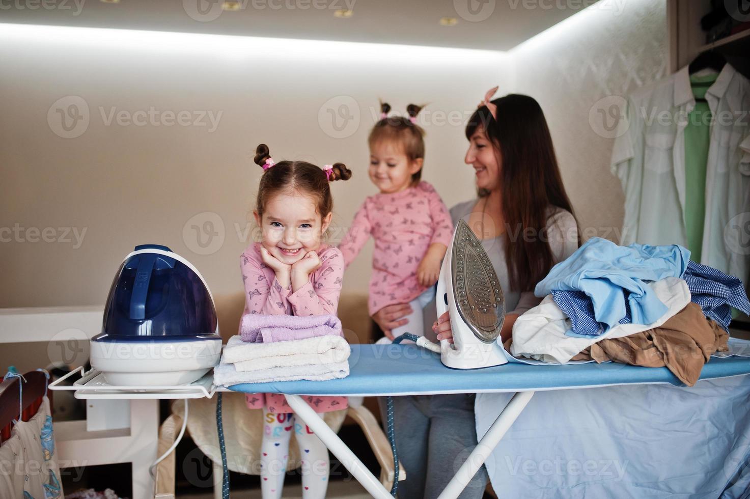 Woman mother and her two daughters child girls as little helper ironing at home. photo