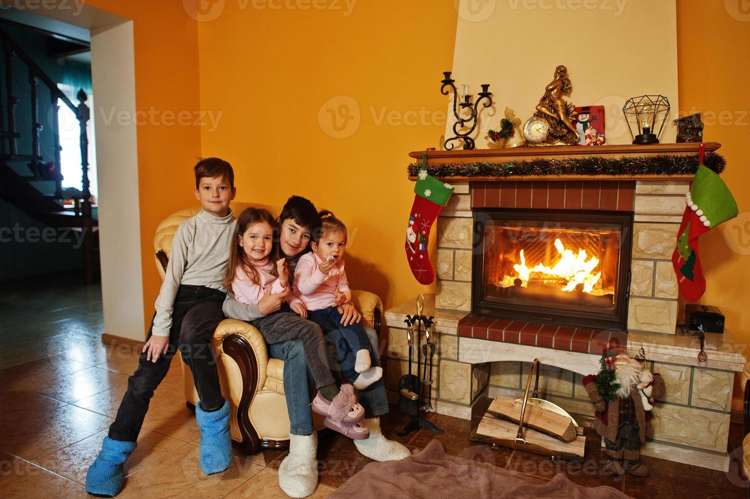 felices cuatro niños en casa junto a una chimenea en una cálida sala de estar el día de invierno. foto