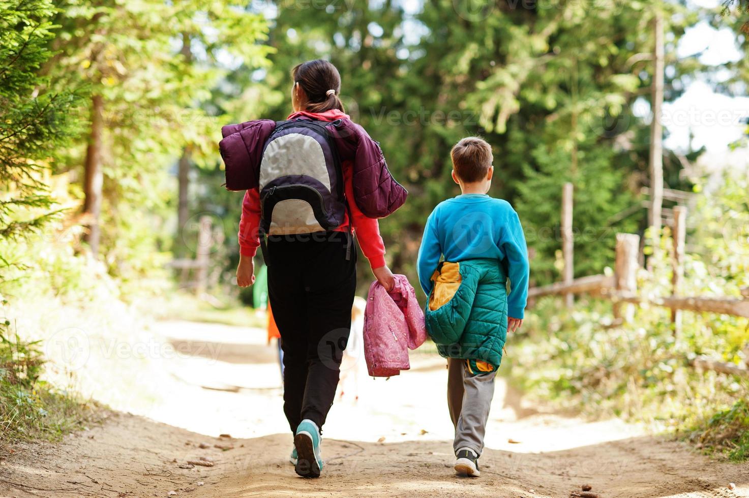 espalda de madre con tres hijos caminando sobre montañas de madera. viajes familiares y senderismo con niños. foto