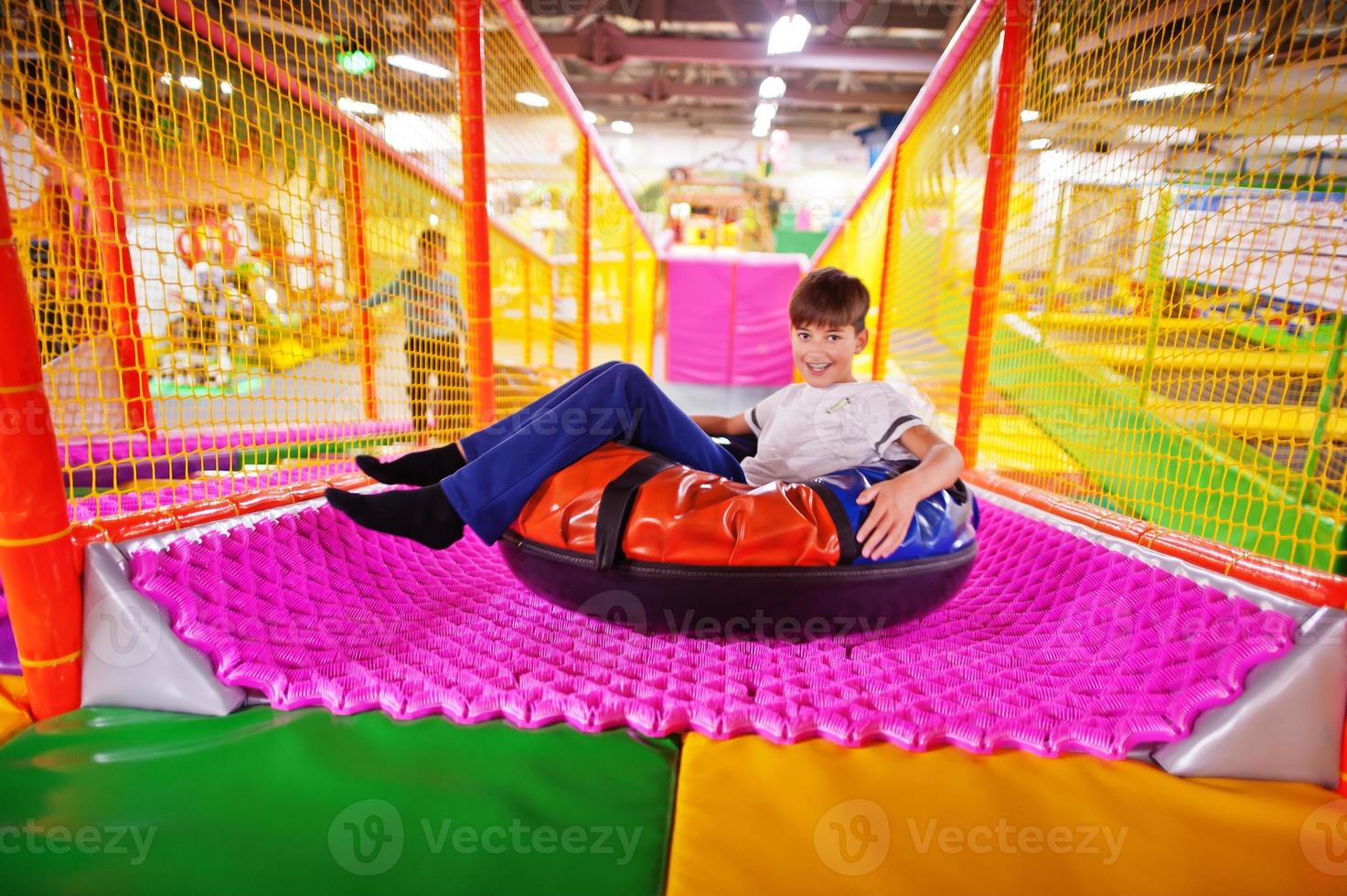 niño feliz sentado en rosquillas disfrutando de toboganes en un divertido centro infantil. foto