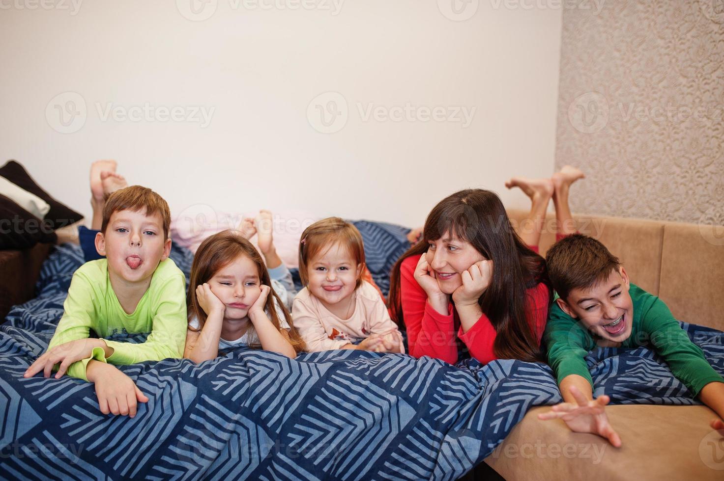 Happy big family is having fun together in bedroom. Large family morning concept. Mother with four kids wear pajamas in bed at home. photo