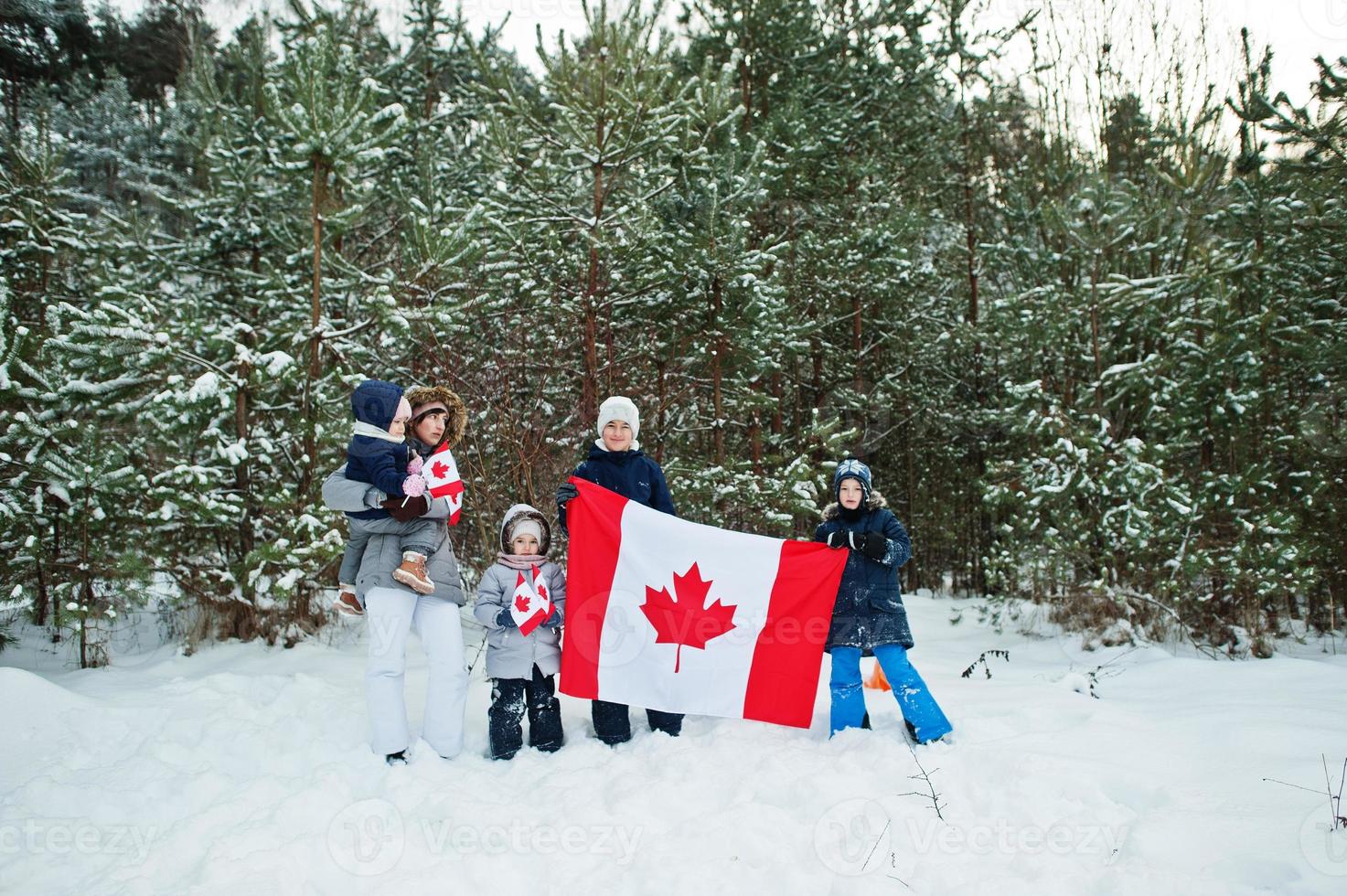 Mother with kids holding flag of Canada on winter landscape. photo