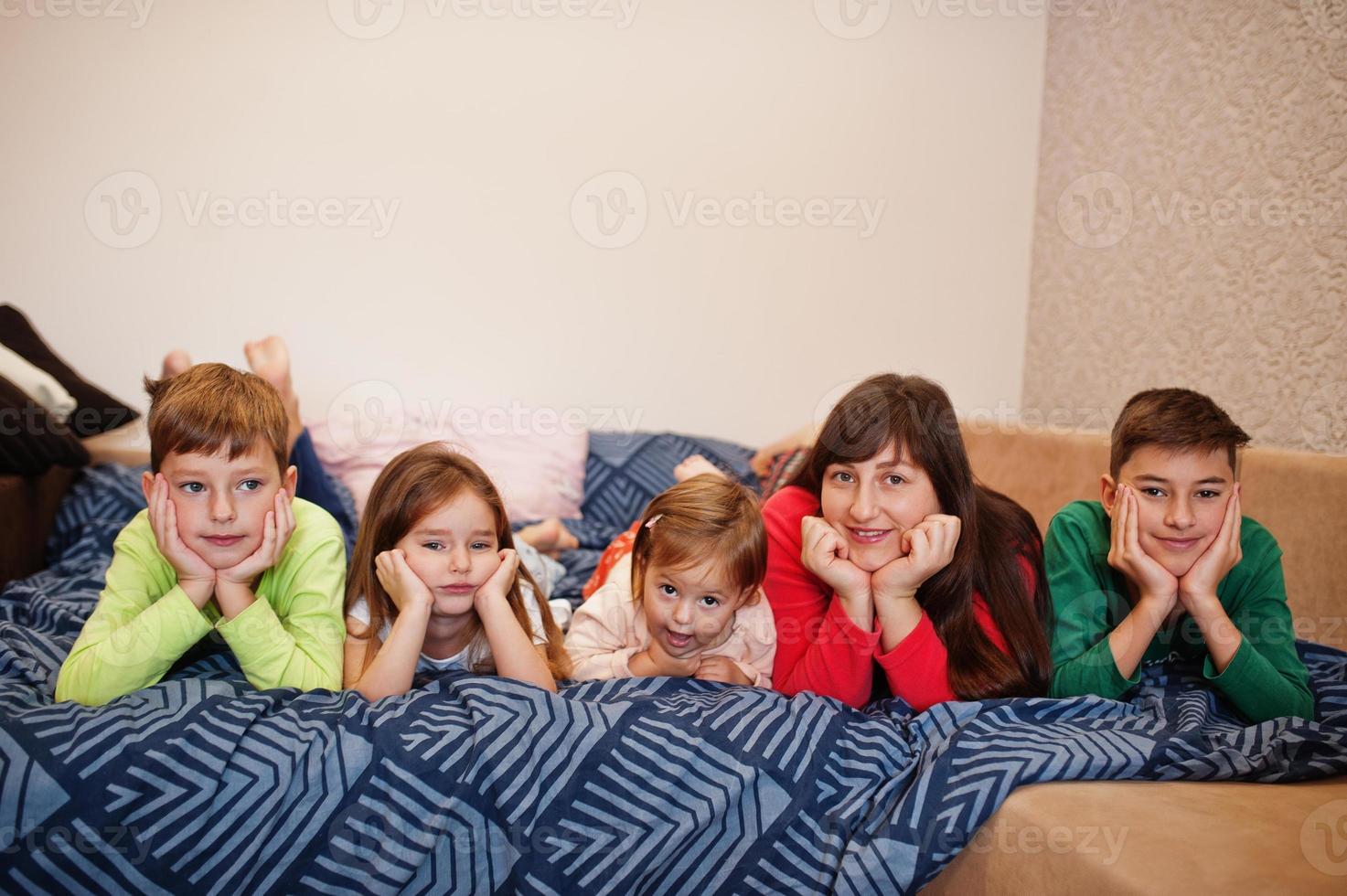 la gran familia feliz se está divirtiendo juntos en el dormitorio. gran concepto de mañana familiar. madre con cuatro hijos usa pijama en la cama en casa. foto