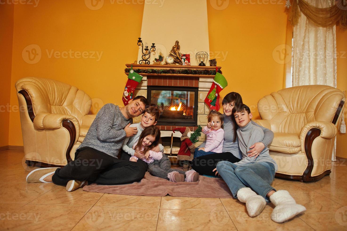 Happy young large family at home by a fireplace in warm living room on winter day. photo