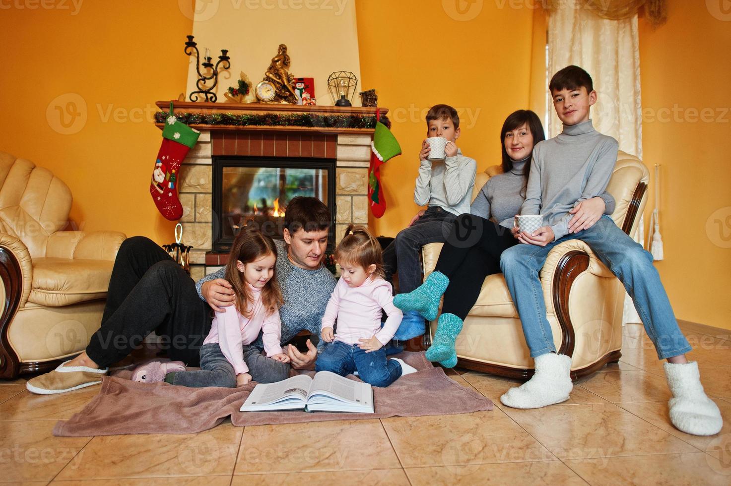 Happy young large family at home by a fireplace in warm living room on winter day. photo