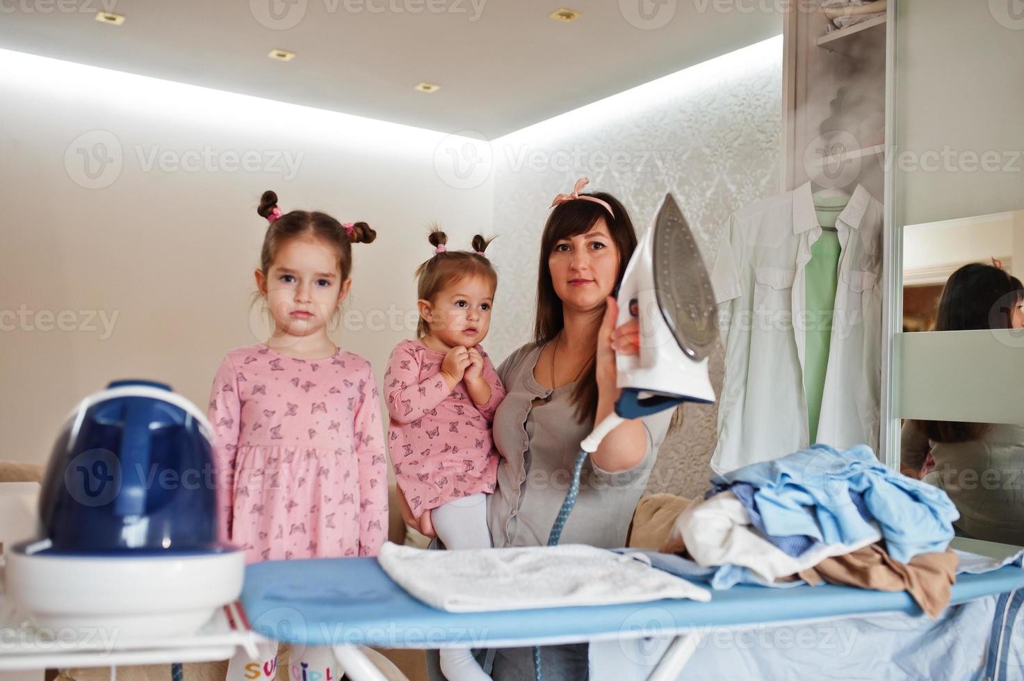 Woman mother and her two daughters child girls as little helper ironing at home. photo