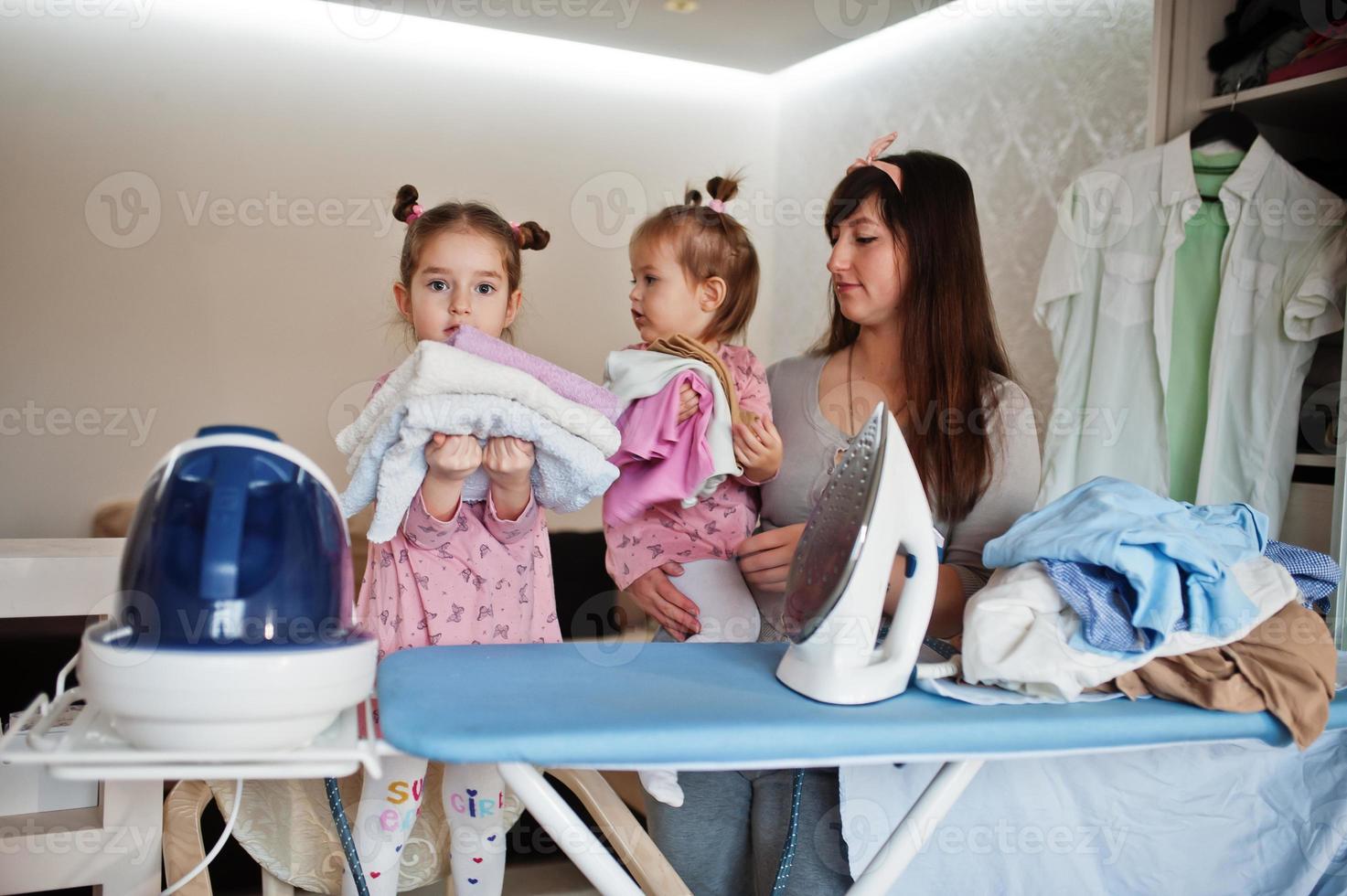 Woman mother and her two daughters child girls as little helper ironing at home. photo