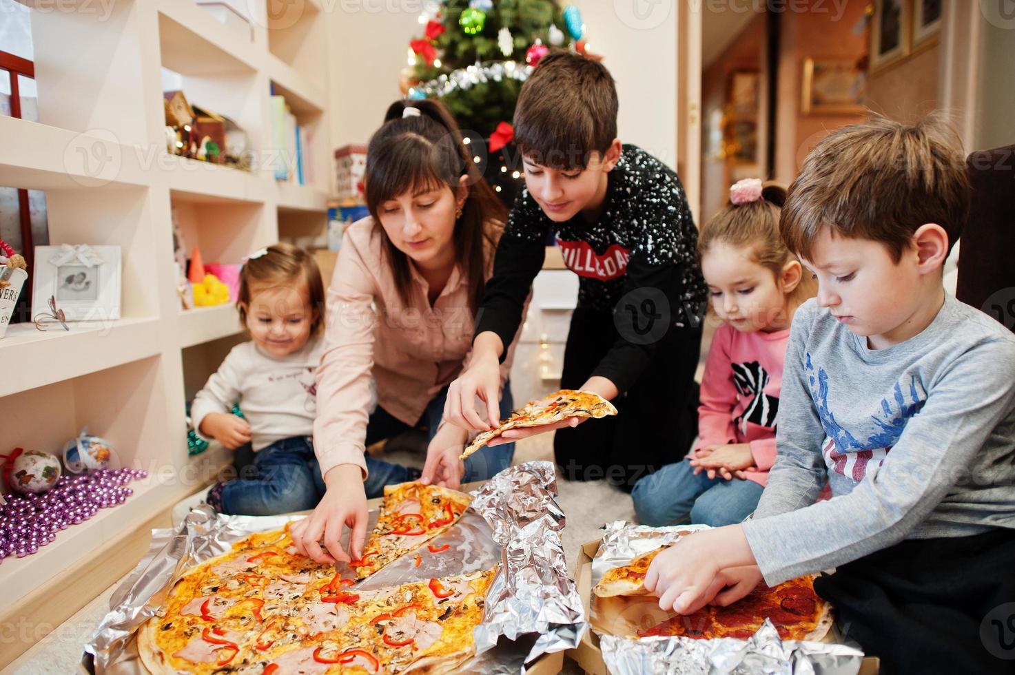 familia feliz con cuatro hijos comiendo pizza en casa. foto