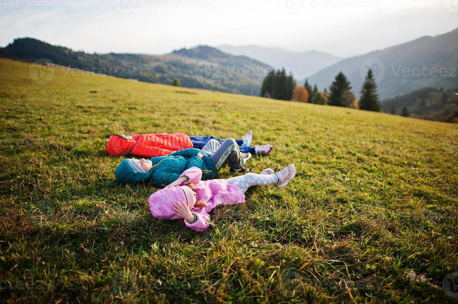 Three kids lying in the grass with a gorgeous mountain range in the horizon. photo