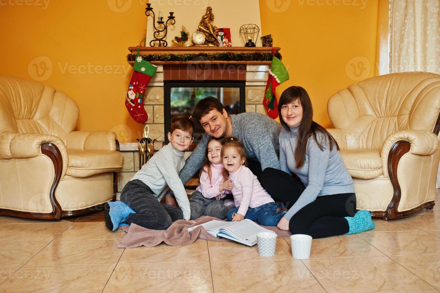 Happy young large family at home by a fireplace in warm living room on winter day. photo